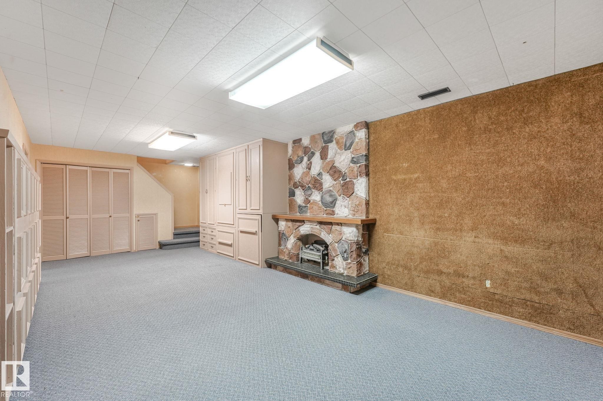 Spacious room featuring a stone-clad fireplace with a wood mantel, light blue carpeting, and built-in cabinetry - 13320 79 Avenue Nw, Edmonton, AB - Indoor Photo Showing Other Room