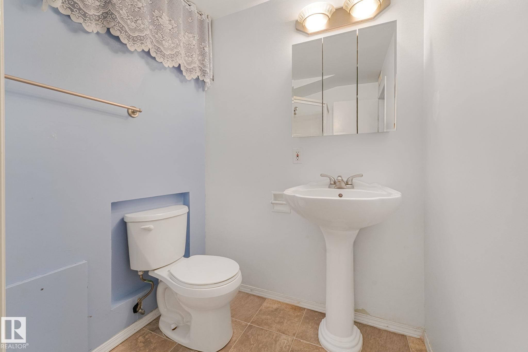 Bathroom featuring a white pedestal sink with a dual-handle faucet, a triple mirrored medicine cabinet, and overhead vanity lighting - 13320 79 Avenue Nw, Edmonton, AB - Indoor Photo Showing Bathroom