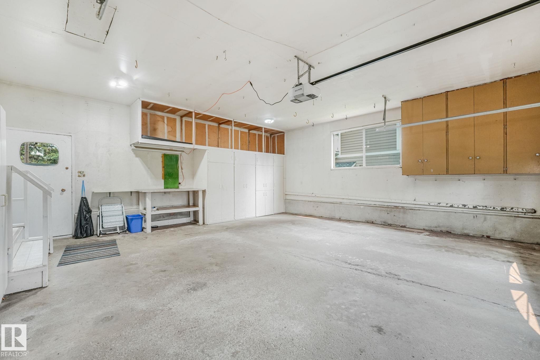 Spacious garage featuring a concrete floor, built-in cabinetry, a workbench, and a multi-pane window for natural light - 13320 79 Avenue Nw, Edmonton, AB - Indoor Photo Showing Garage