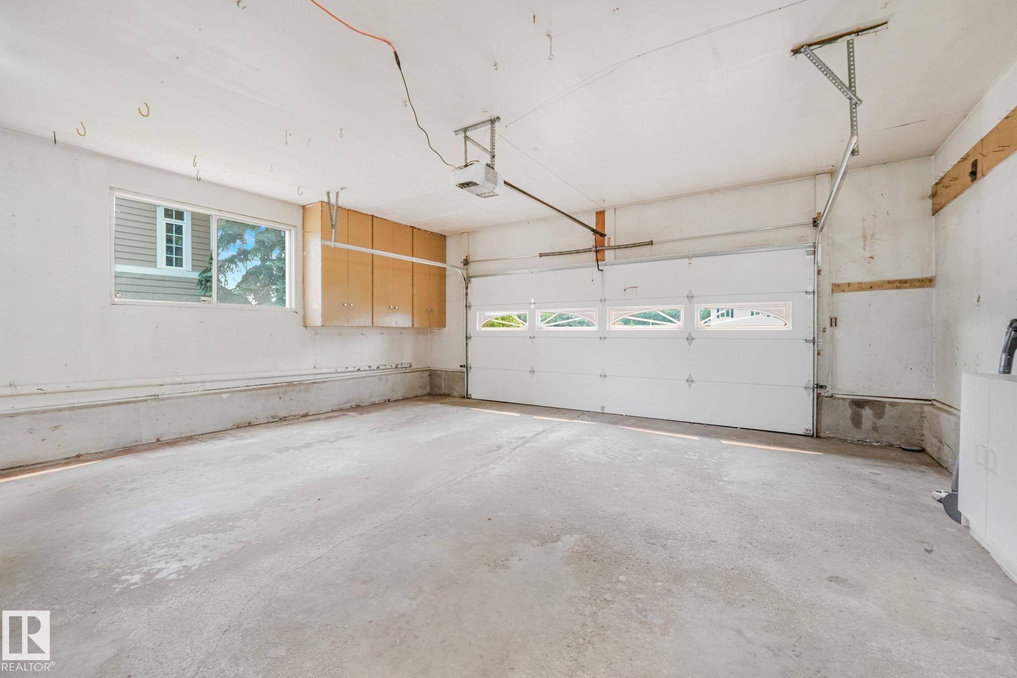 Spacious garage featuring a concrete floor, overhead door with window inserts, automatic garage door opener, built-in cabinetry, and an exterior window - 13320 79 Avenue Nw, Edmonton, AB - Indoor Photo Showing Garage