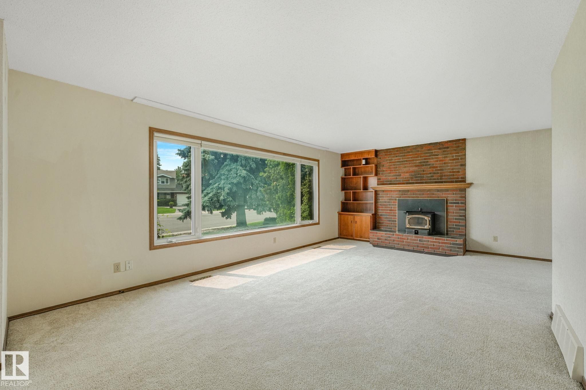 Living area featuring a large picture window, a brick fireplace with a wood-burning insert, and built-in wood shelving with cabinetry - 13320 79 Avenue Nw, Edmonton, AB - Indoor Photo Showing Living Room With Fireplace