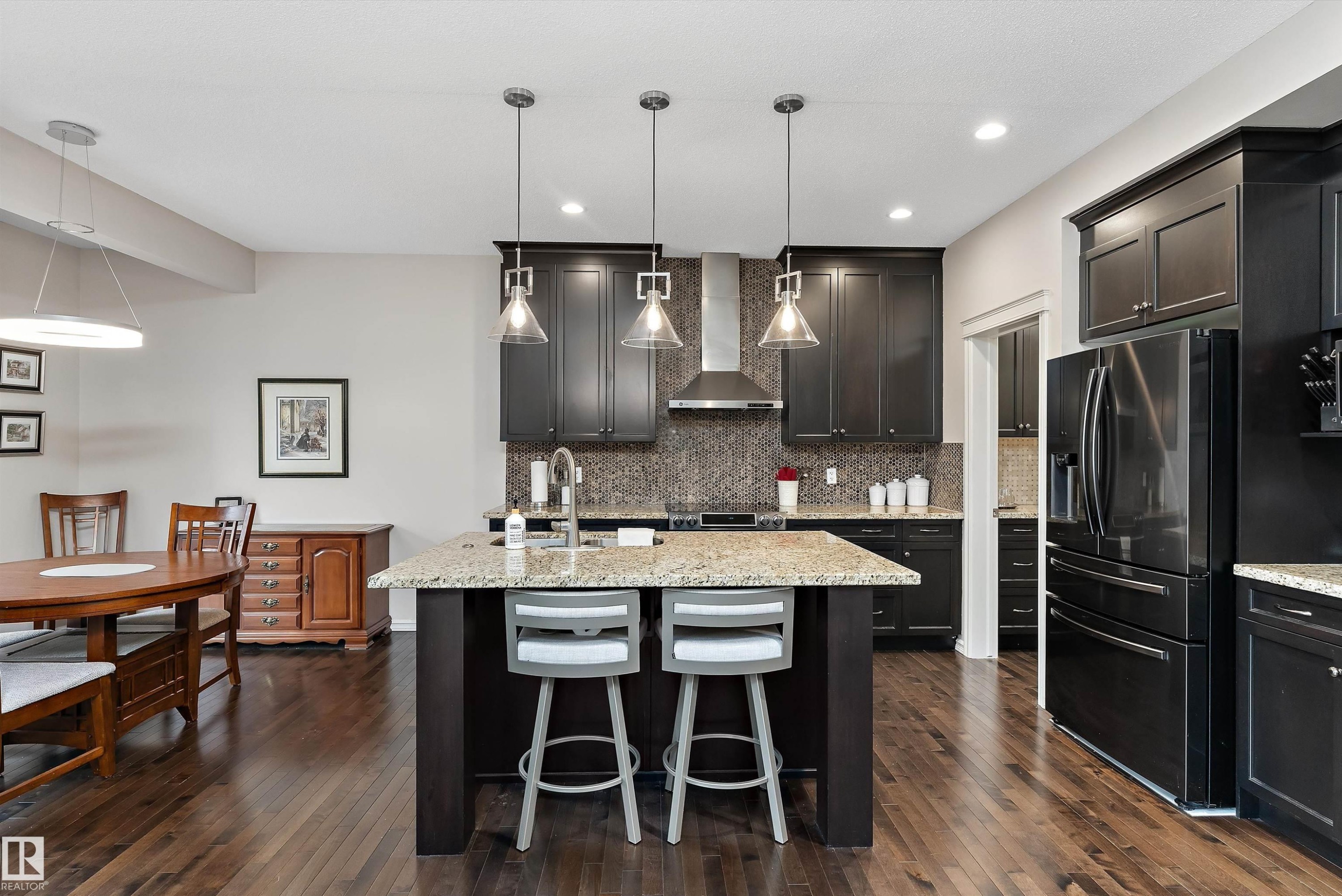 Gourmet kitchen featuring dark wood cabinetry, stainless steel appliances, granite countertops, a large center island with seating, and wood-finish flooring - 1097 Armitage Crescent, Edmonton, AB