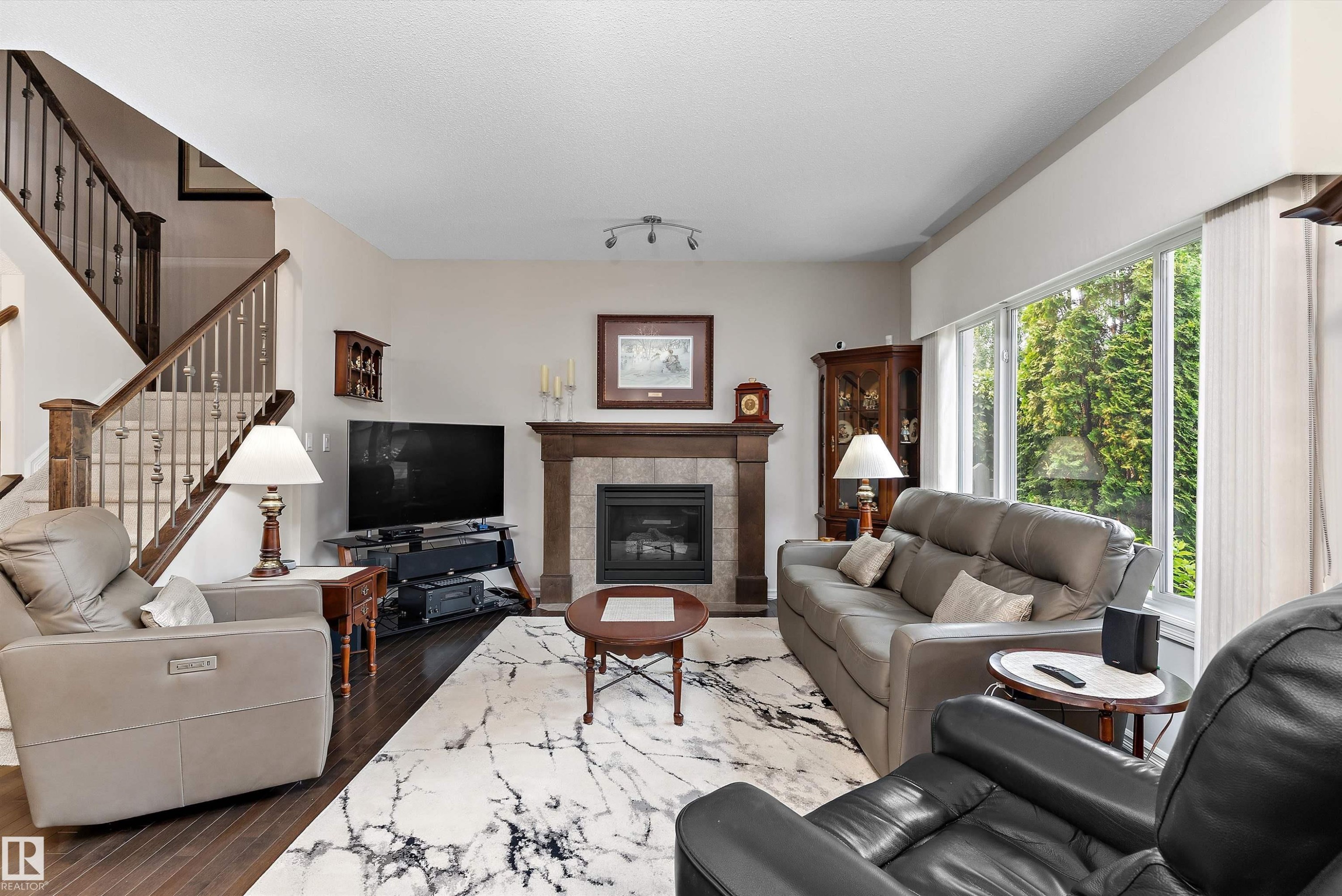 Spacious living area featuring wood-finish flooring, a contemporary fireplace with a wood mantle and stone tile surround, and large picture windows - 1097 Armitage Crescent, Edmonton, AB