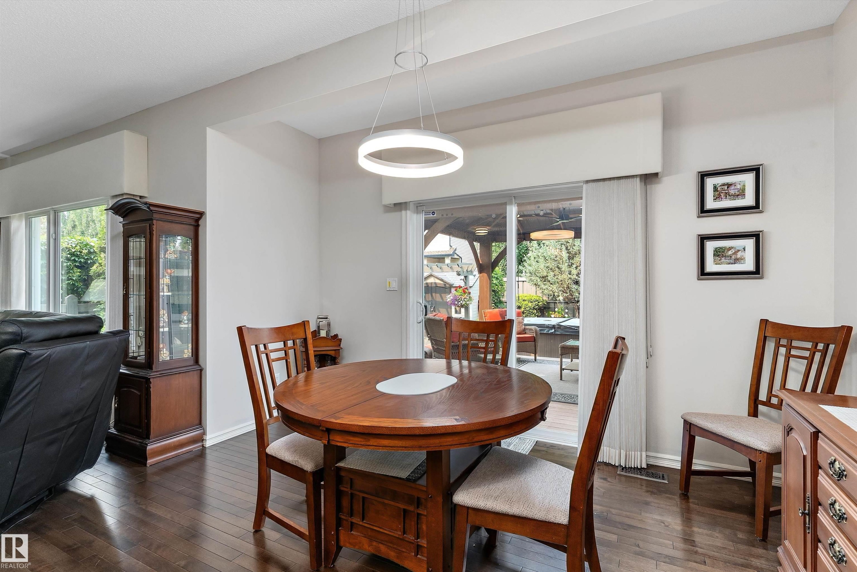 Dining area with dark wood-finish flooring, a contemporary circular light fixture, and a glass sliding door providing access to the exterior space - 1097 Armitage Crescent, Edmonton, AB