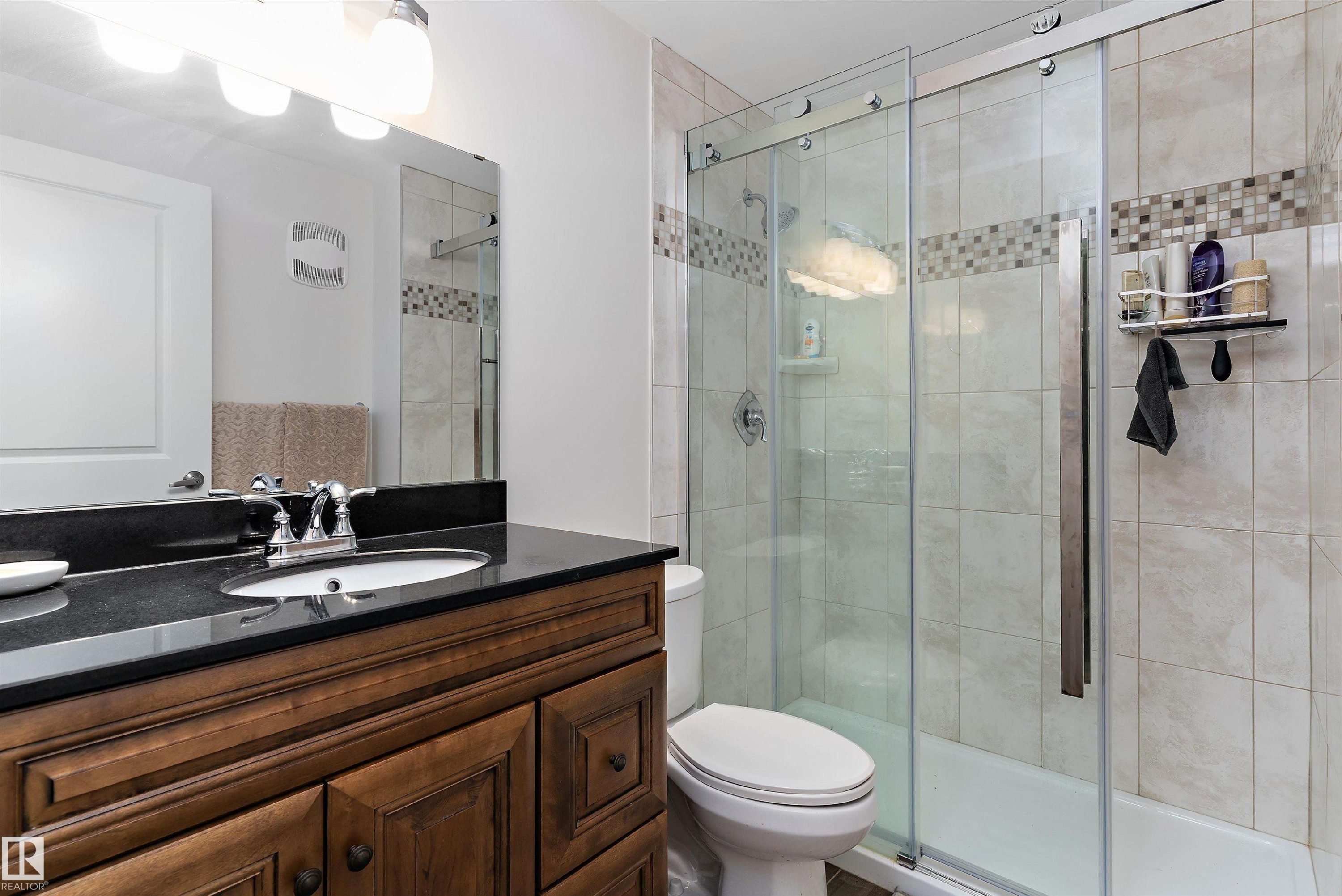 Bathroom featuring a wood-finish vanity with a built-in sink, a dark countertop, and a chrome faucet - 1097 Armitage Crescent, Edmonton, AB