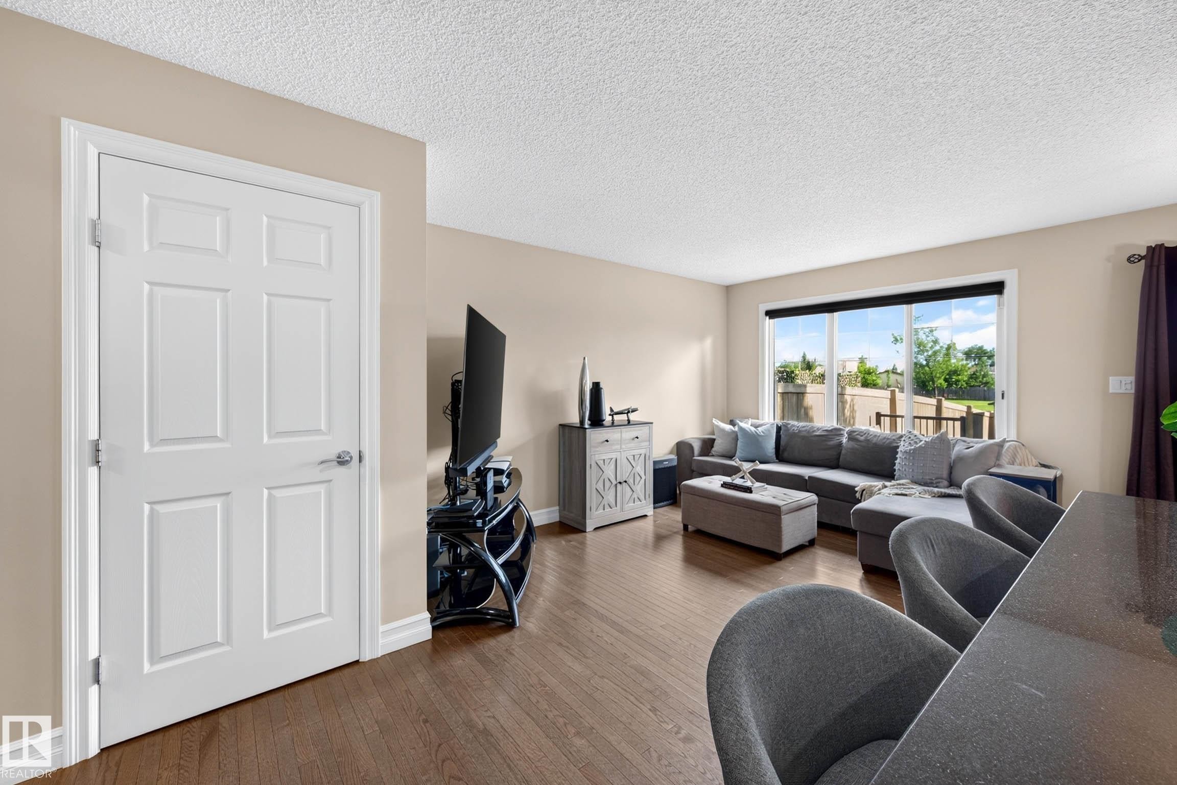 Living area featuring wood-finish flooring, light beige wall paint, white trim, and a white six-panel door - 12119 167A Avenue, Edmonton, AB