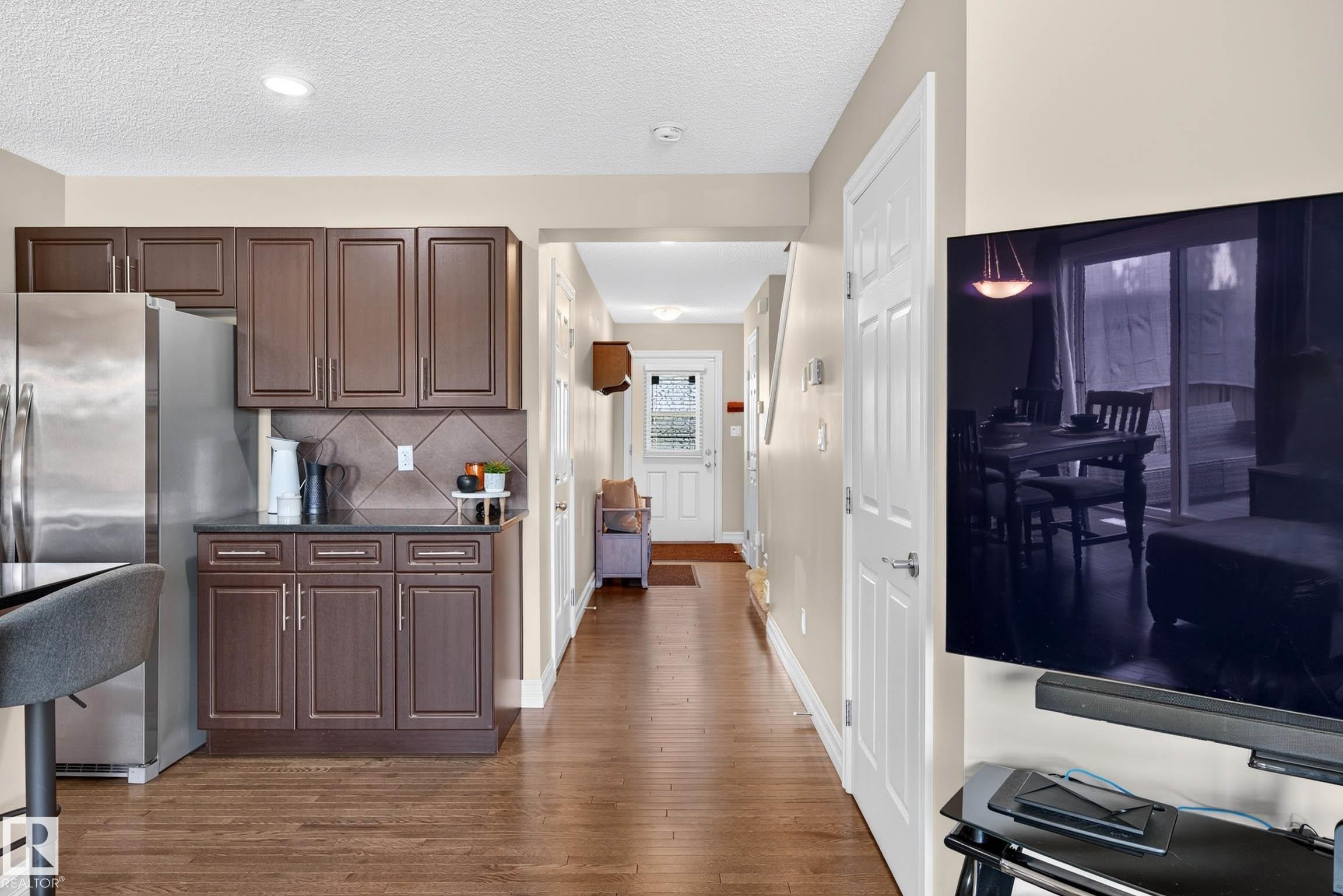 Kitchen with dark wood-finish cabinetry, stainless steel refrigerator, and dark countertop with tiled backsplash - 12119 167A Avenue, Edmonton, AB