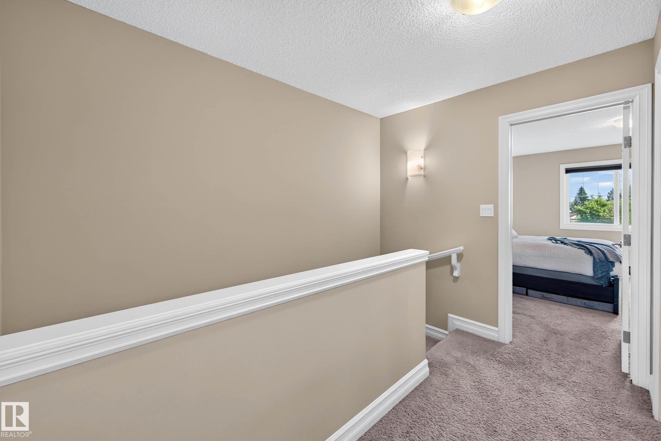 Carpeted hallway with neutral wall paint and white trim, featuring a wall sconce and recessed ceiling light - 12119 167A Avenue, Edmonton, AB