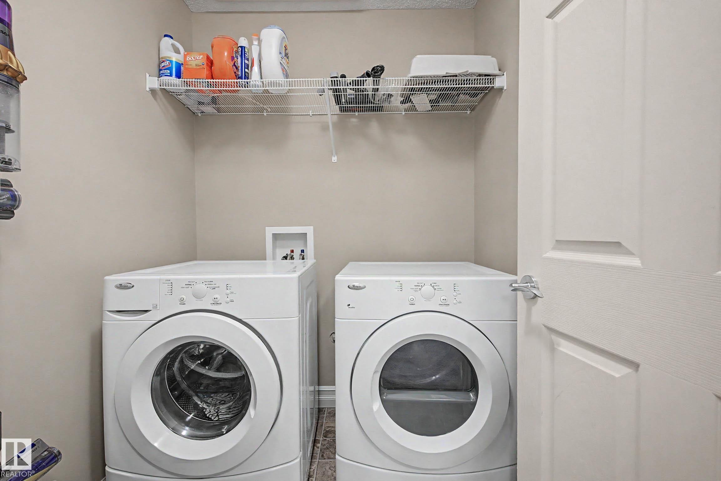 Dedicated laundry area featuring a front-load washer and dryer set, neutral wall color, wire shelving, and wood-finish flooring - 12119 167A Avenue, Edmonton, AB