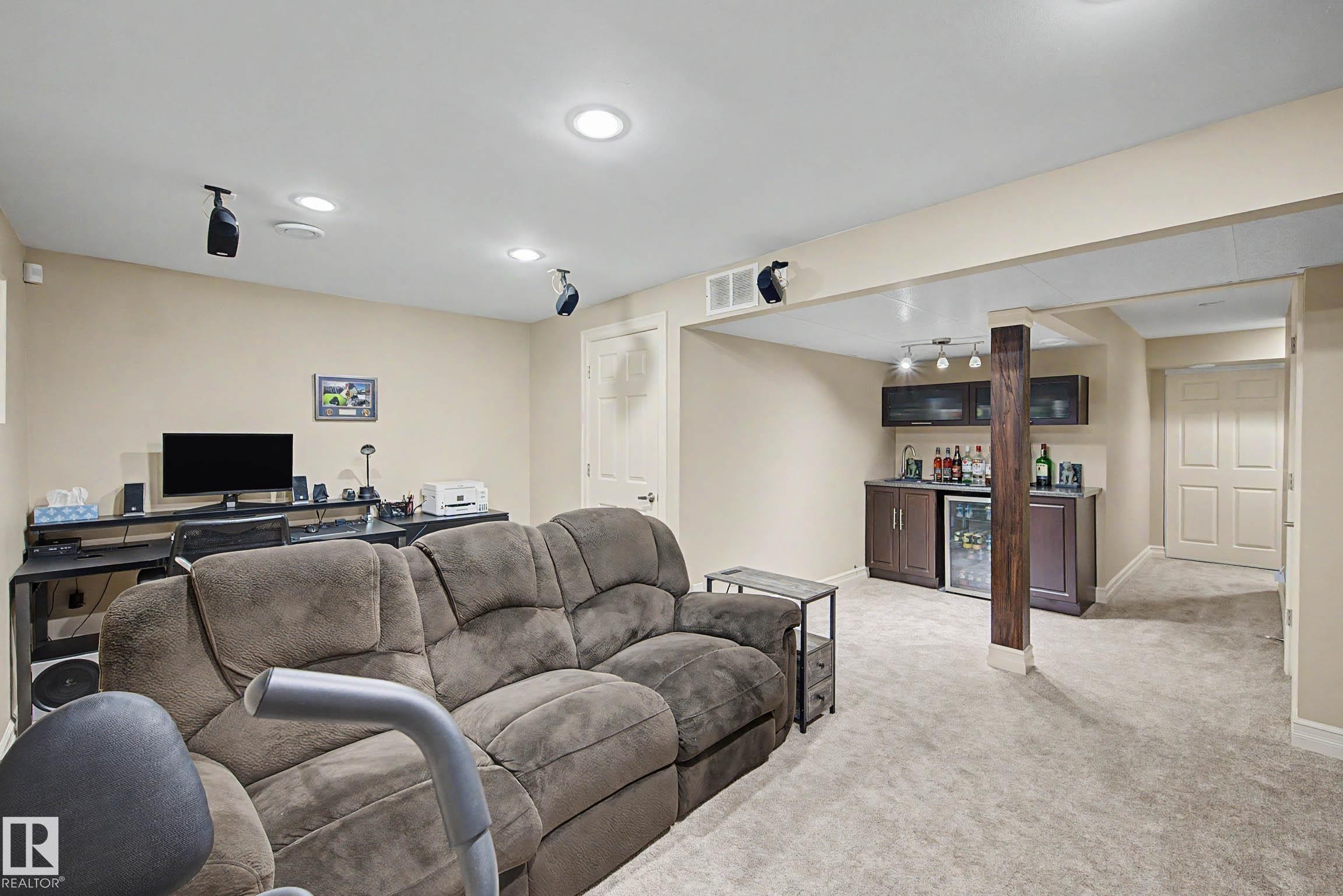Finished lower level featuring recessed lighting, a built-in wet bar with dark cabinetry and stainless steel beverage cooler, light-toned carpeting, and a white paneled door - 12119 167A Avenue, Edmonton, AB