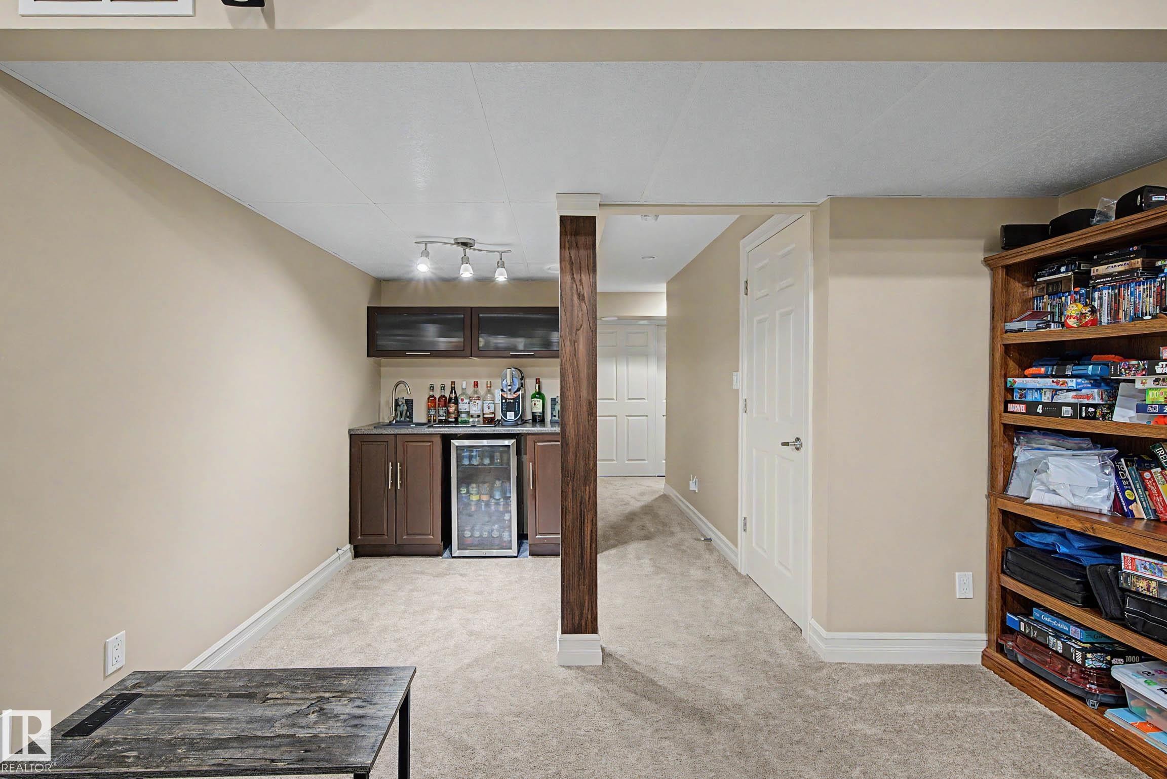 Basement recreation area featuring a built-in wet bar with dark cabinetry, track lighting, and a beverage cooler - 12119 167A Avenue, Edmonton, AB