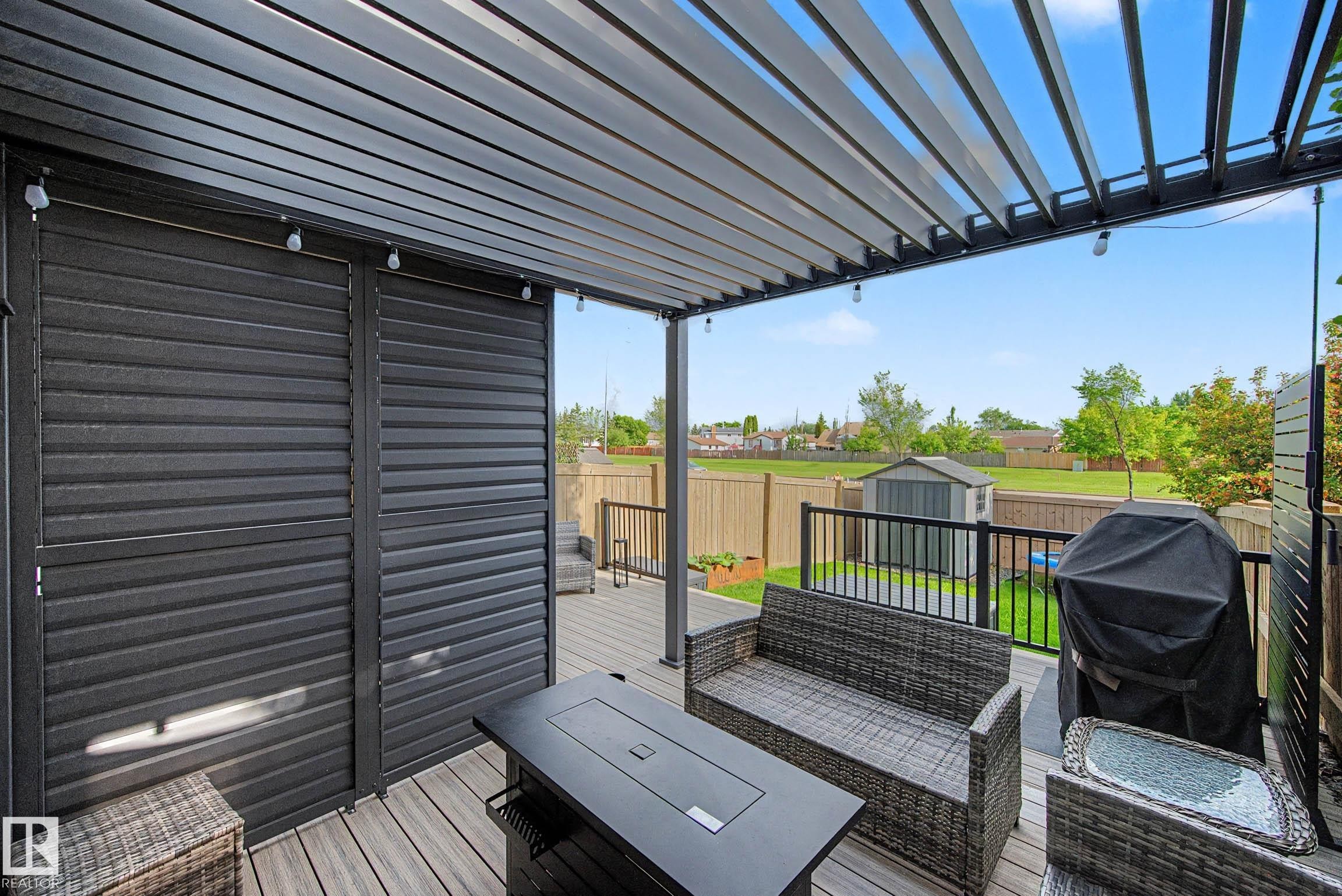 Expansive outdoor deck featuring a louvered pergola with integrated lighting, wood-finish decking, and black metal railings - 12119 167A Avenue, Edmonton, AB