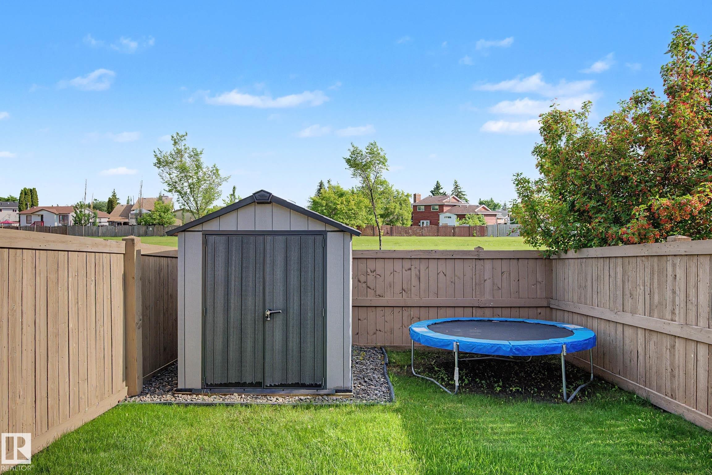 Private backyard featuring a storage shed on a gravel base, bordered by wood fencing and a manicured lawn - 12119 167A Avenue, Edmonton, AB