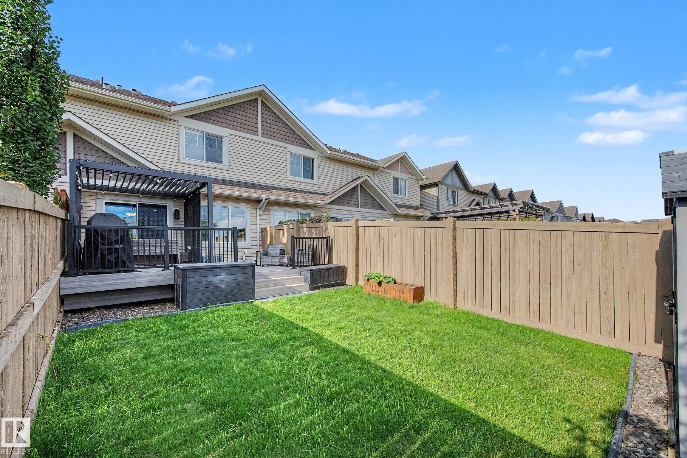 Fenced backyard featuring a wooden deck with a black pergola, green lawn, and a small storage shed - 12119 167A Avenue, Edmonton, AB