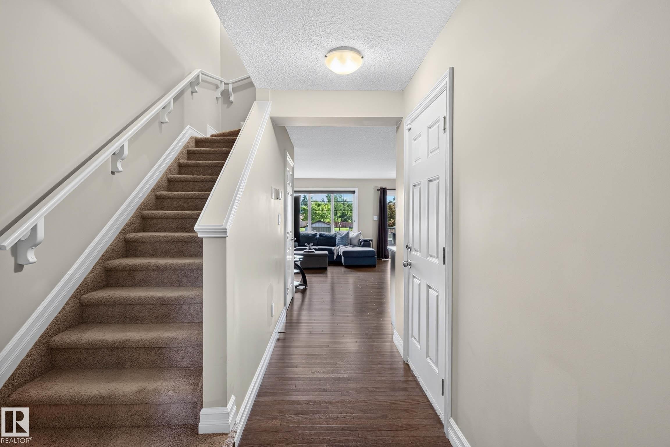 Carpeted staircase with white handrails and trim, complemented by wood-finish flooring extending into the background living space - 12119 167A Avenue, Edmonton, AB