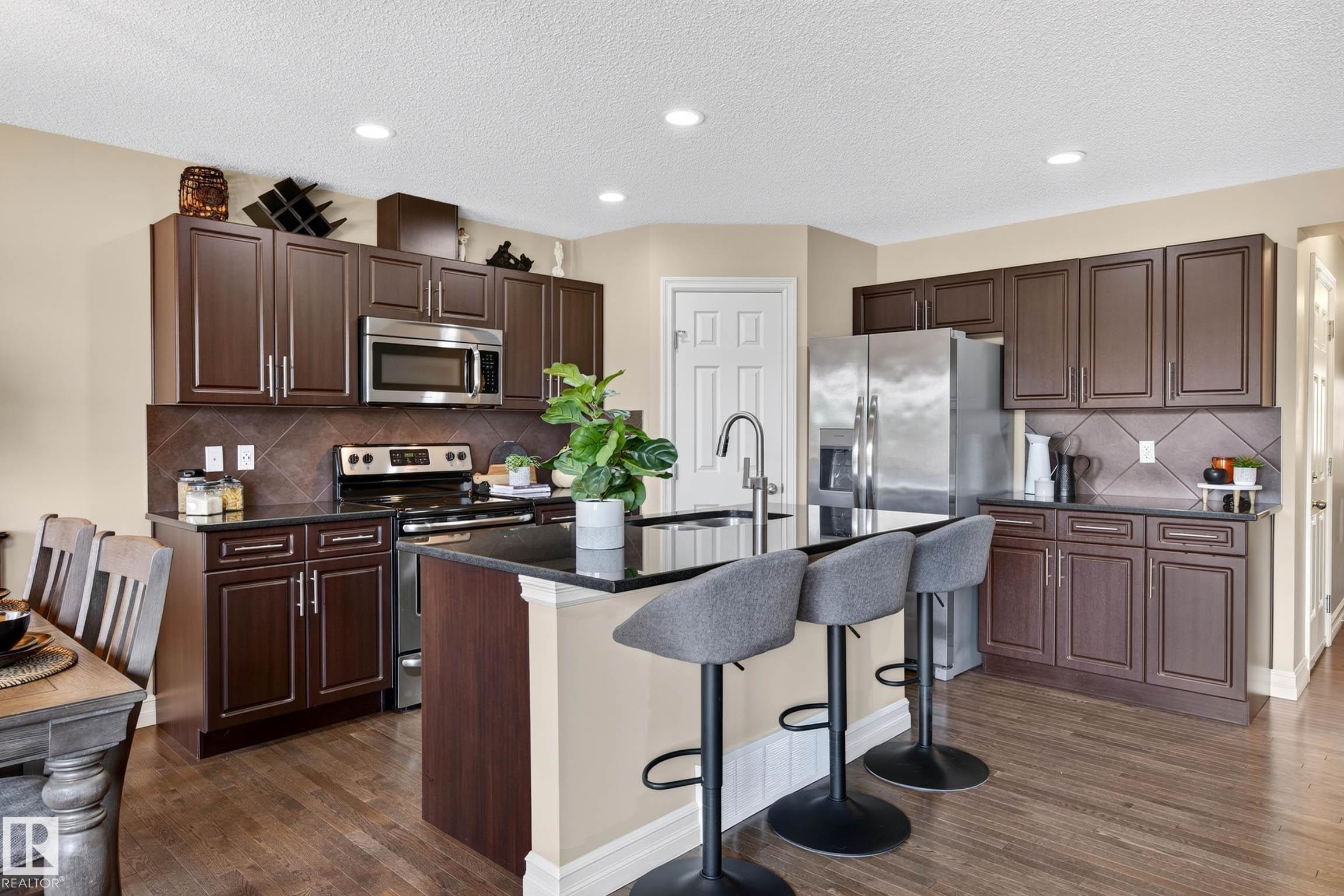 Kitchen featuring dark wood cabinetry, stainless steel appliances, dark countertops, a central island with bar seating, and wood-finish flooring - 12119 167A Avenue, Edmonton, AB