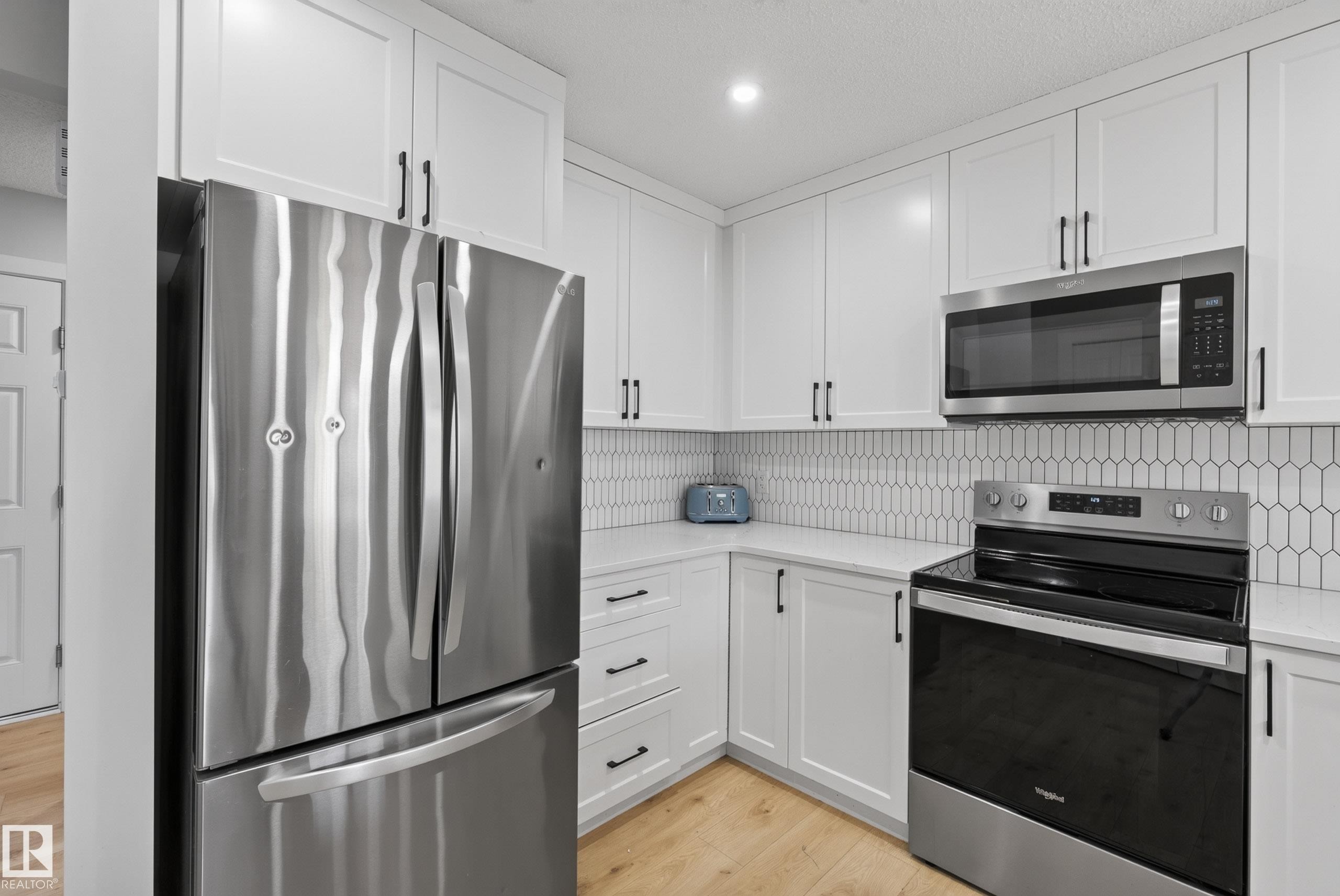 Contemporary kitchen featuring stainless steel appliances, white shaker cabinetry with dark hardware, quartz countertops, and a picket tile backsplash - 5129 Lark Crescent Nw, Edmonton, AB - Indoor Photo Showing Kitchen