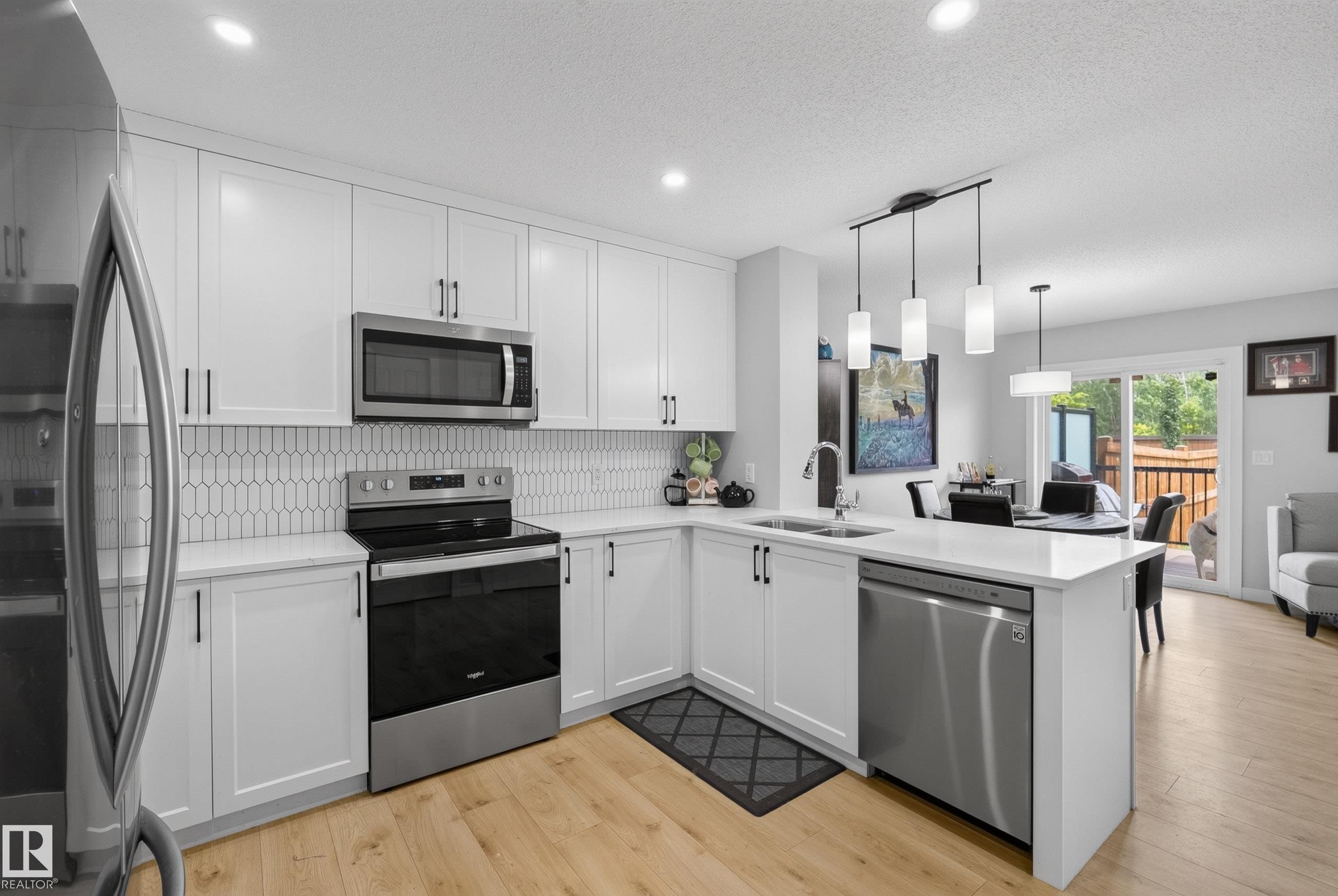 Modern kitchen featuring white cabinetry, stainless steel appliances, a white picket tile backsplash, and light wood-finish flooring - 5129 Lark Crescent Nw, Edmonton, AB - Indoor Photo Showing Kitchen With Double Sink With Upgraded Kitchen