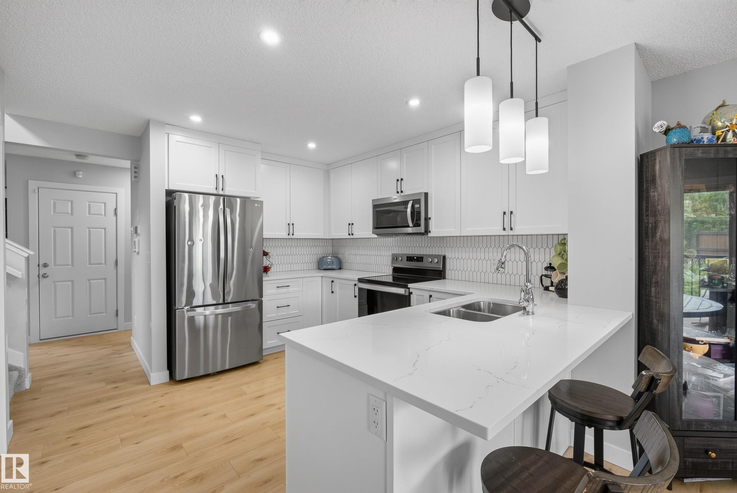 Contemporary kitchen featuring white cabinetry, light-toned wood-finish flooring, and a breakfast bar with a solid surface countertop - 5129 Lark Crescent Nw, Edmonton, AB - Indoor Photo Showing Kitchen With Double Sink With Upgraded Kitchen