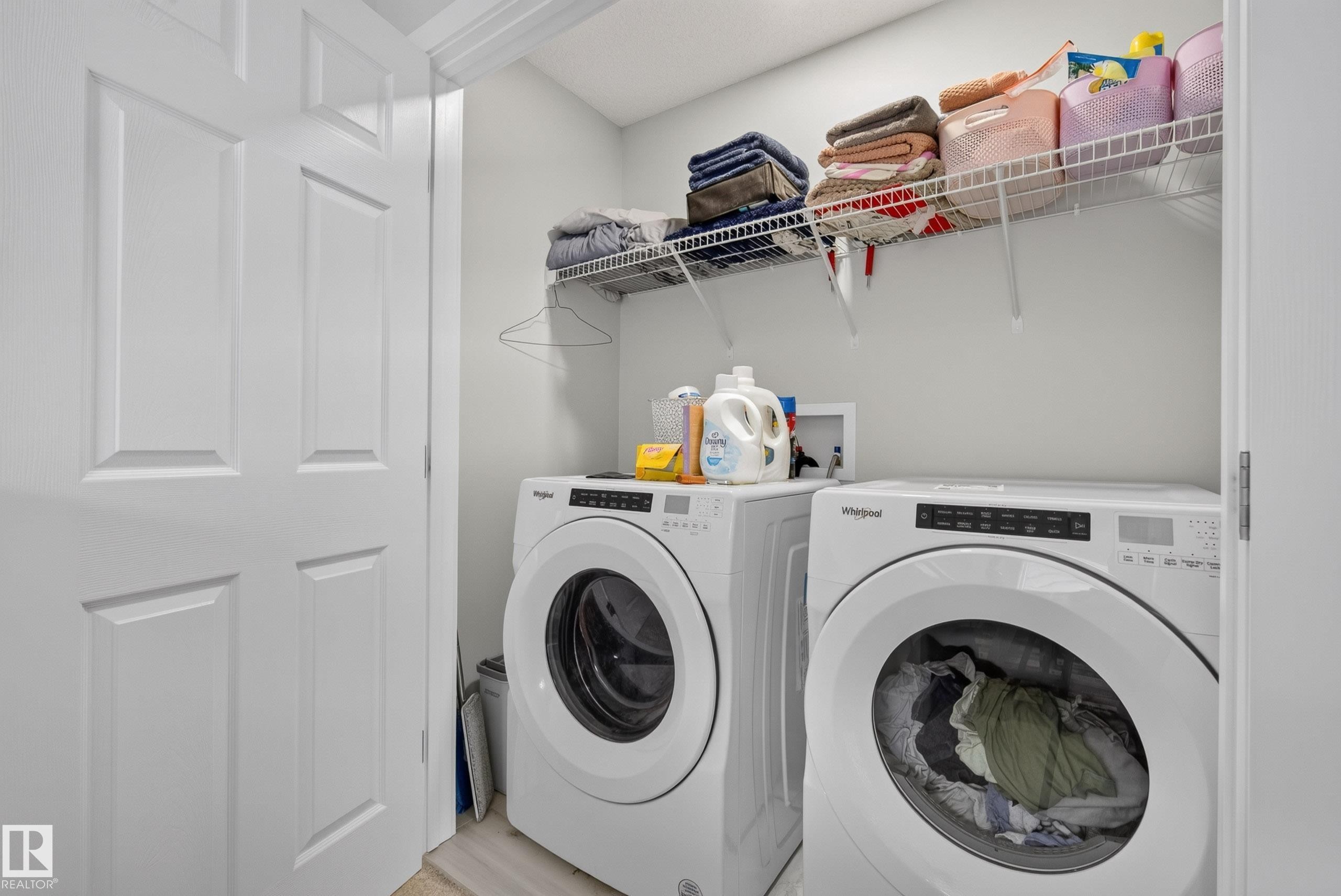 Dedicated laundry area featuring front-loading appliances, overhead wire shelving, and white paneled doors - 5129 Lark Crescent Nw, Edmonton, AB - Indoor Photo Showing Laundry Room