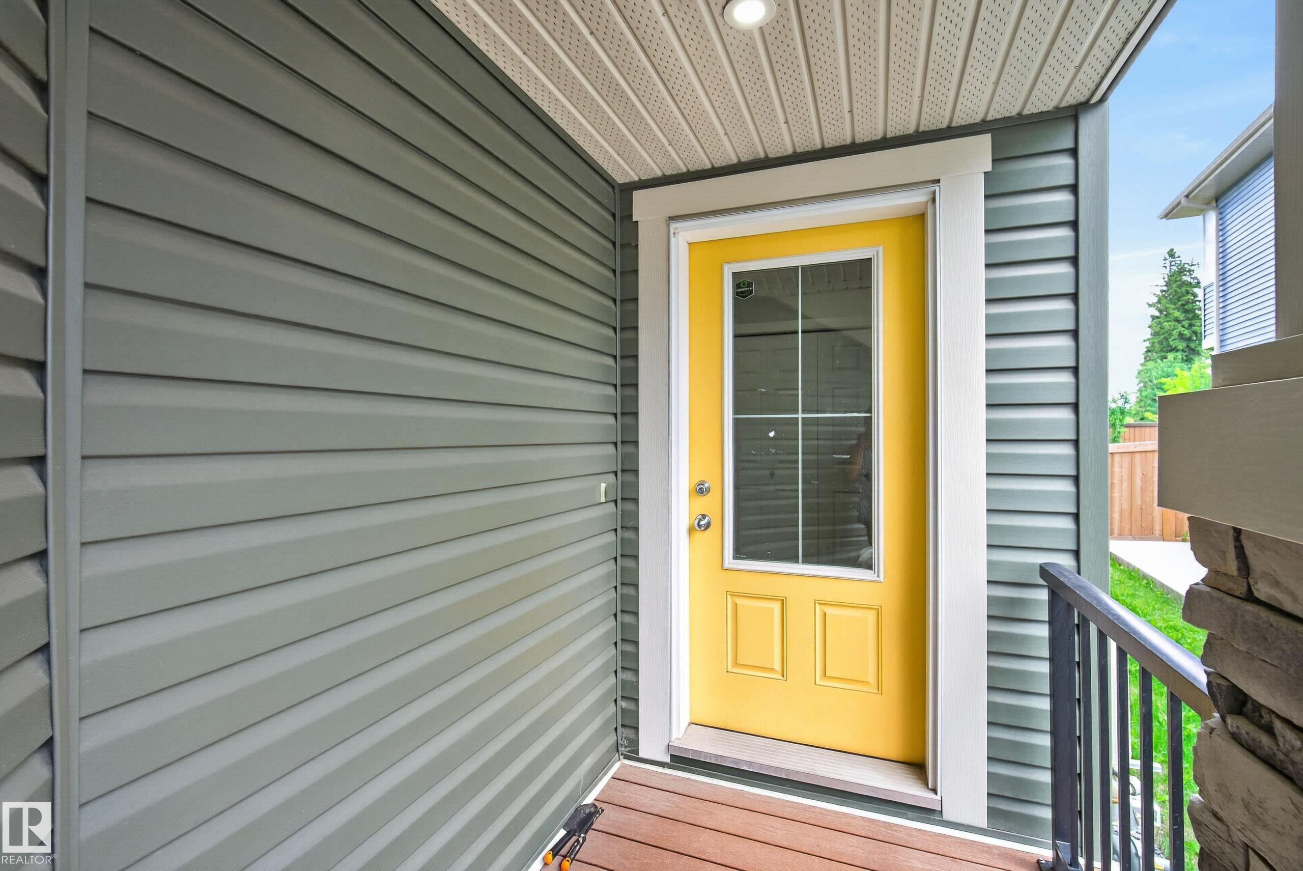 Vibrant yellow entry door with upper glass paneling, set against horizontal grey siding - 5129 Lark Crescent Nw, Edmonton, AB - Outdoor With Exterior