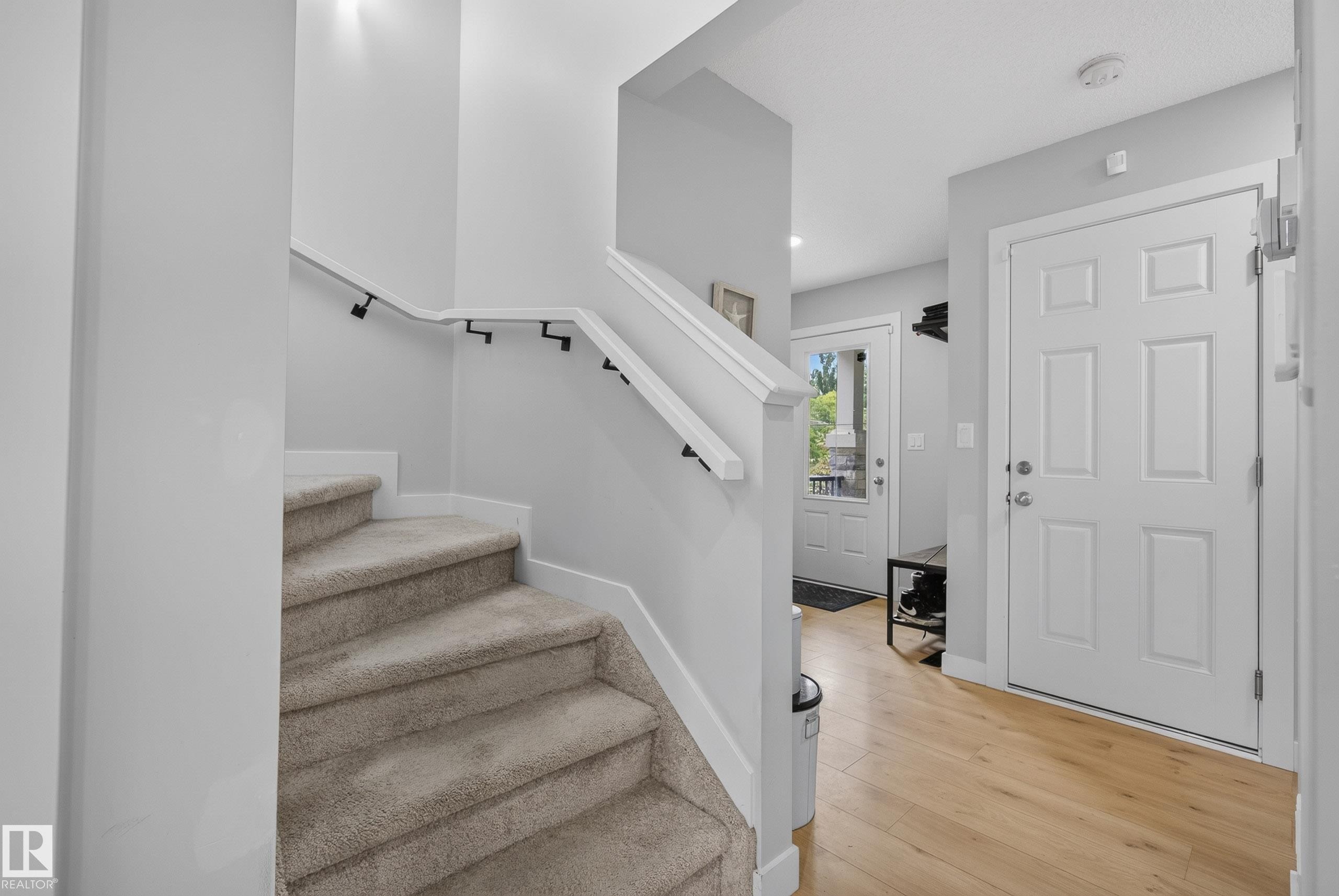Inviting entryway featuring light wood-finish flooring, a six-panel door, and a carpeted staircase with a modern handrail - 5129 Lark Crescent Nw, Edmonton, AB - Indoor Photo Showing Other Room