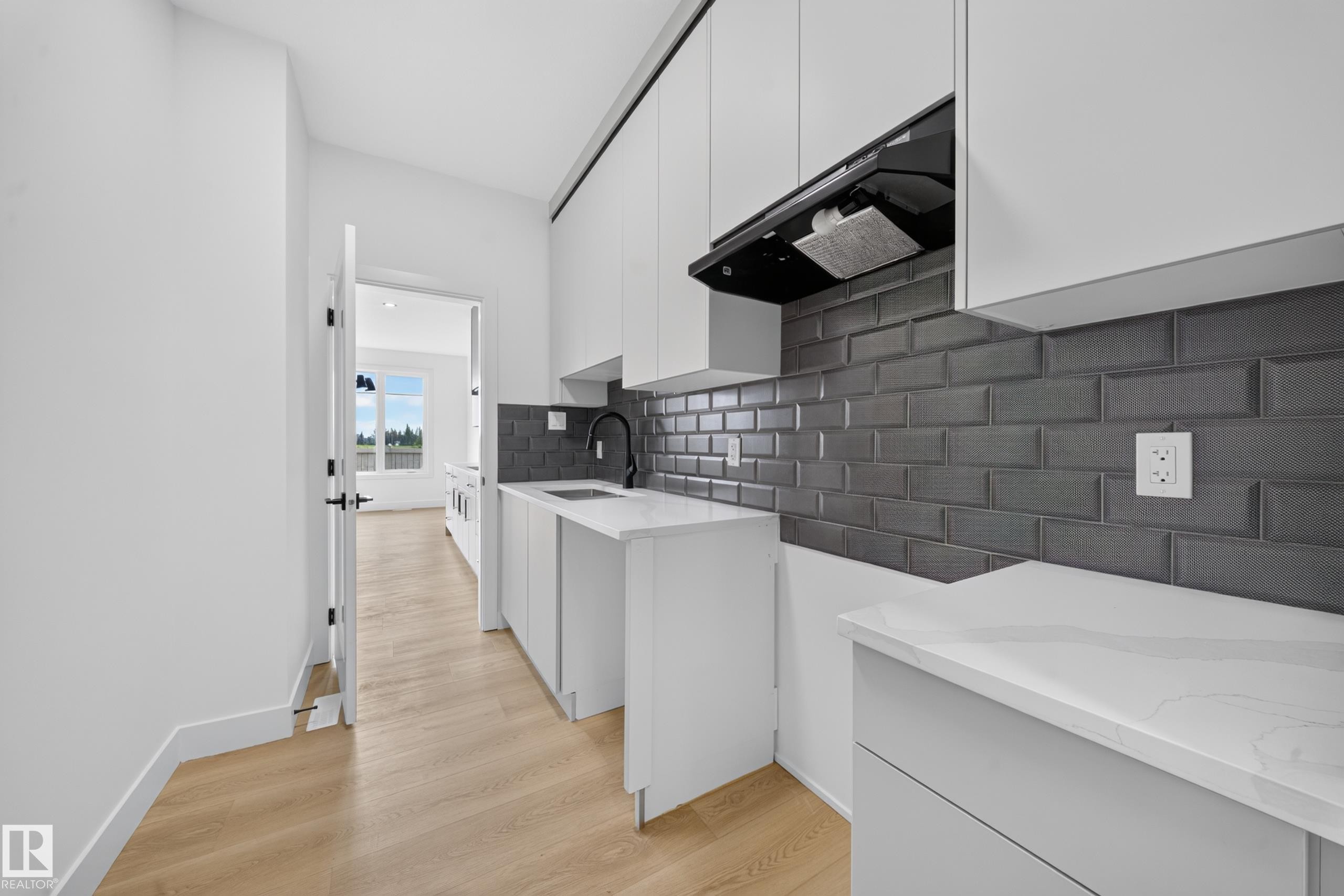 Modern kitchen featuring white flat-panel cabinetry, a dark subway tile backsplash, and light wood-finish flooring - 803 30 Avenue, Edmonton, AB
