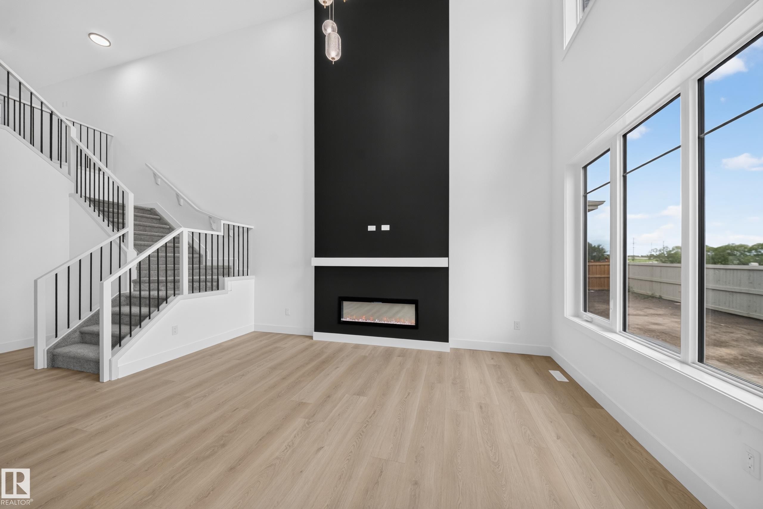 Two-story living area featuring a full-height black accent wall with an integrated linear fireplace, light wood-finish flooring, and a contemporary staircase with black iron spindles - 803 30 Avenue, Edmonton, AB