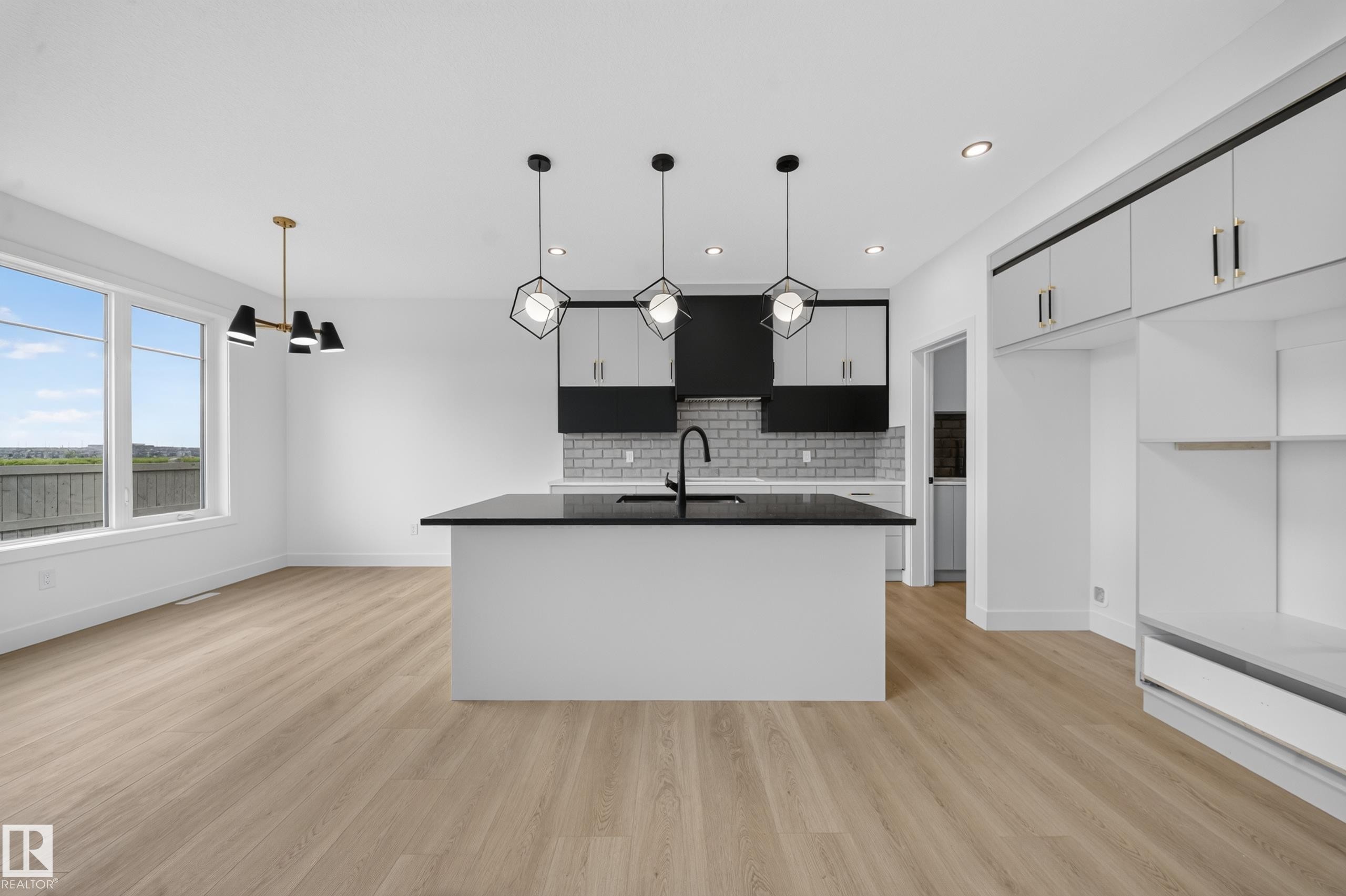 Open-concept kitchen and dining area featuring light wood-finish flooring, a kitchen island with pendant lighting, a subway tile backsplash, stainless steel appliances, and large windows - 803 30 Avenue, Edmonton, AB