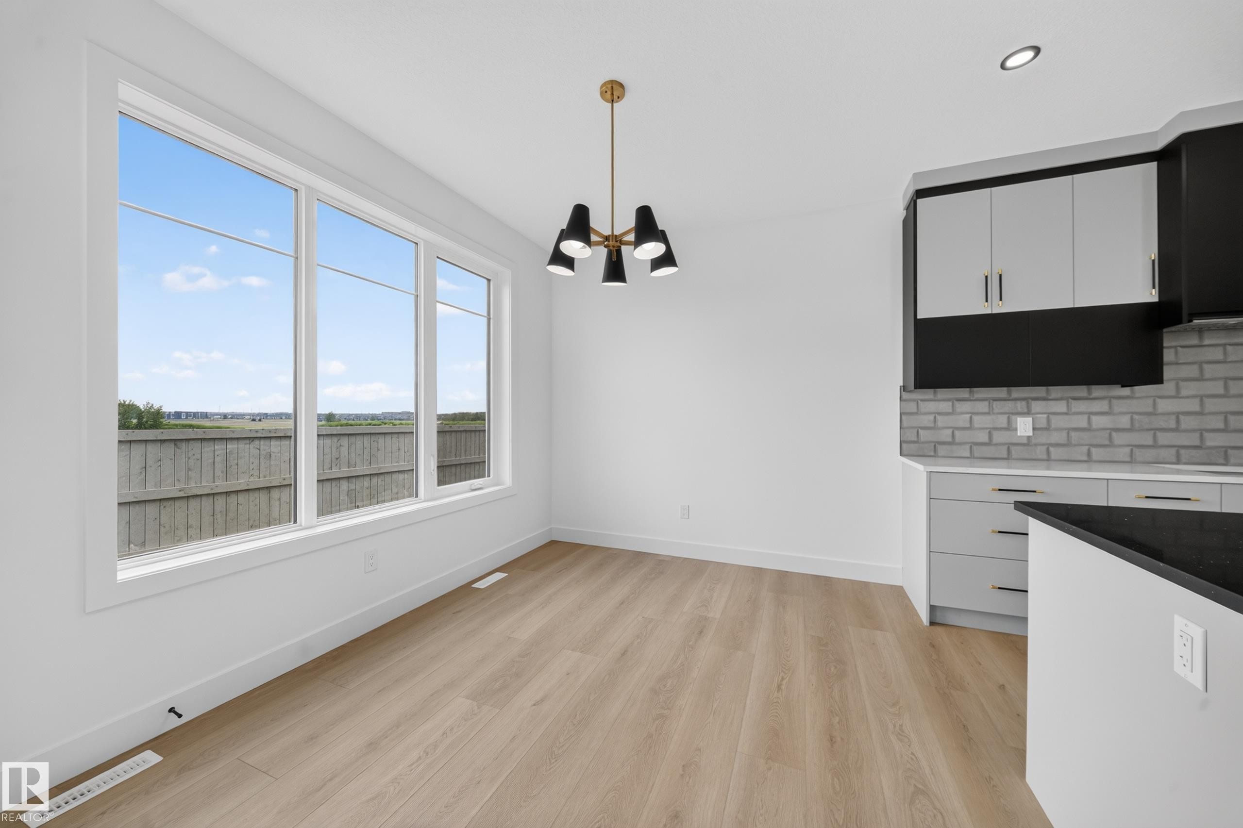 Kitchen featuring a large island with a black sink and faucet, light wood-finish flooring, white cabinetry with black accents, a light gray brick-patterned backsplash, and modern pendant lighting - 803 30 Avenue, Edmonton, AB