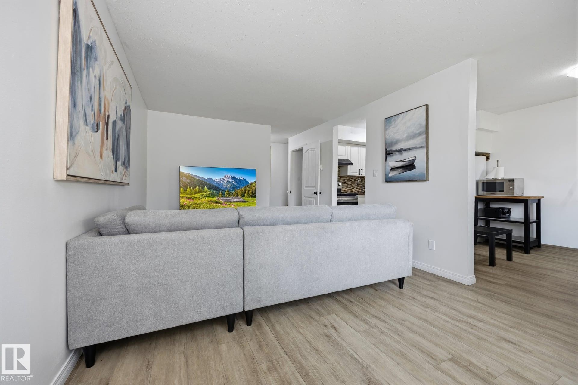 Open-concept living area featuring wood-finish flooring and white walls - 105 16428 109 Street, Edmonton, AB
