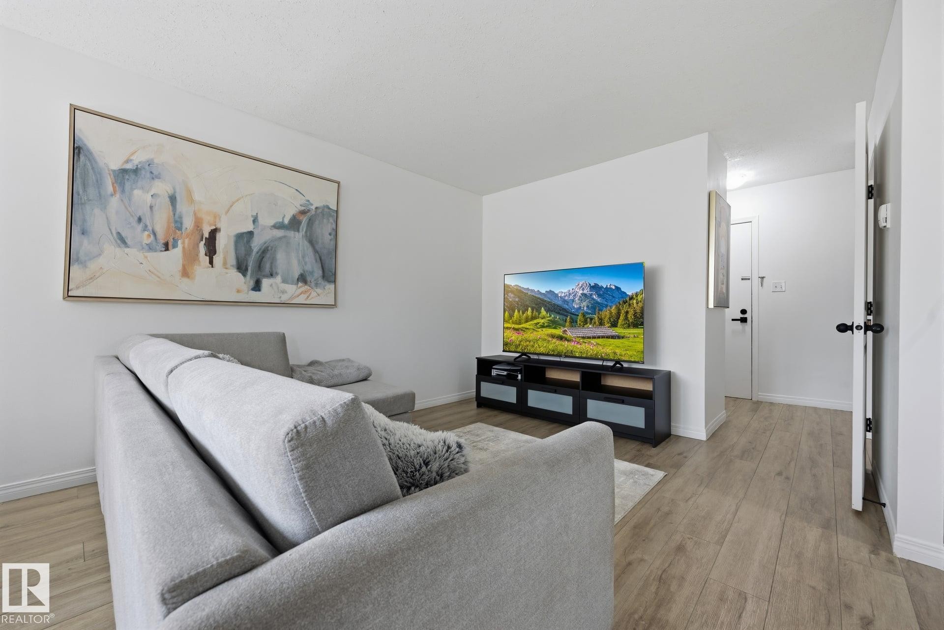 Open-concept living space featuring wood-finish flooring, white walls, and contemporary black door hardware - 105 16428 109 Street, Edmonton, AB
