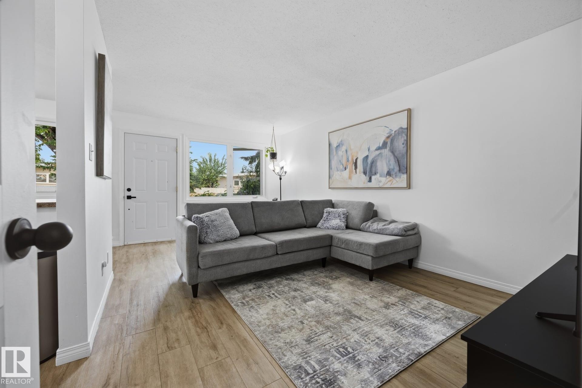 Living area featuring wood-finish flooring, white walls, and multiple windows allowing natural light - 105 16428 109 Street, Edmonton, AB