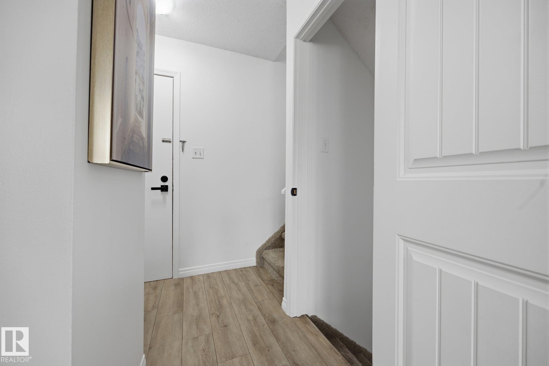 Hallway featuring wood-finish flooring, white trim, and a staircase with carpeted treads - 105 16428 109 Street, Edmonton, AB