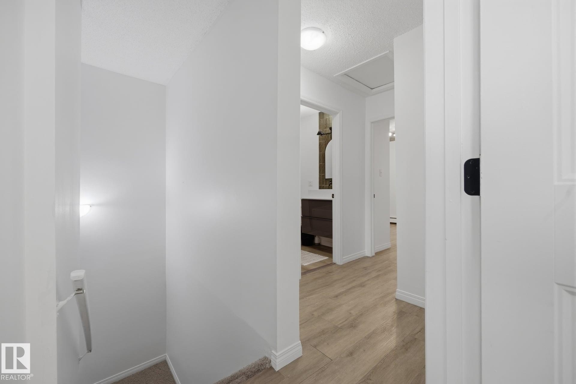 Hallway featuring wood-finish flooring, white painted walls, and ceiling-mounted lighting - 105 16428 109 Street, Edmonton, AB