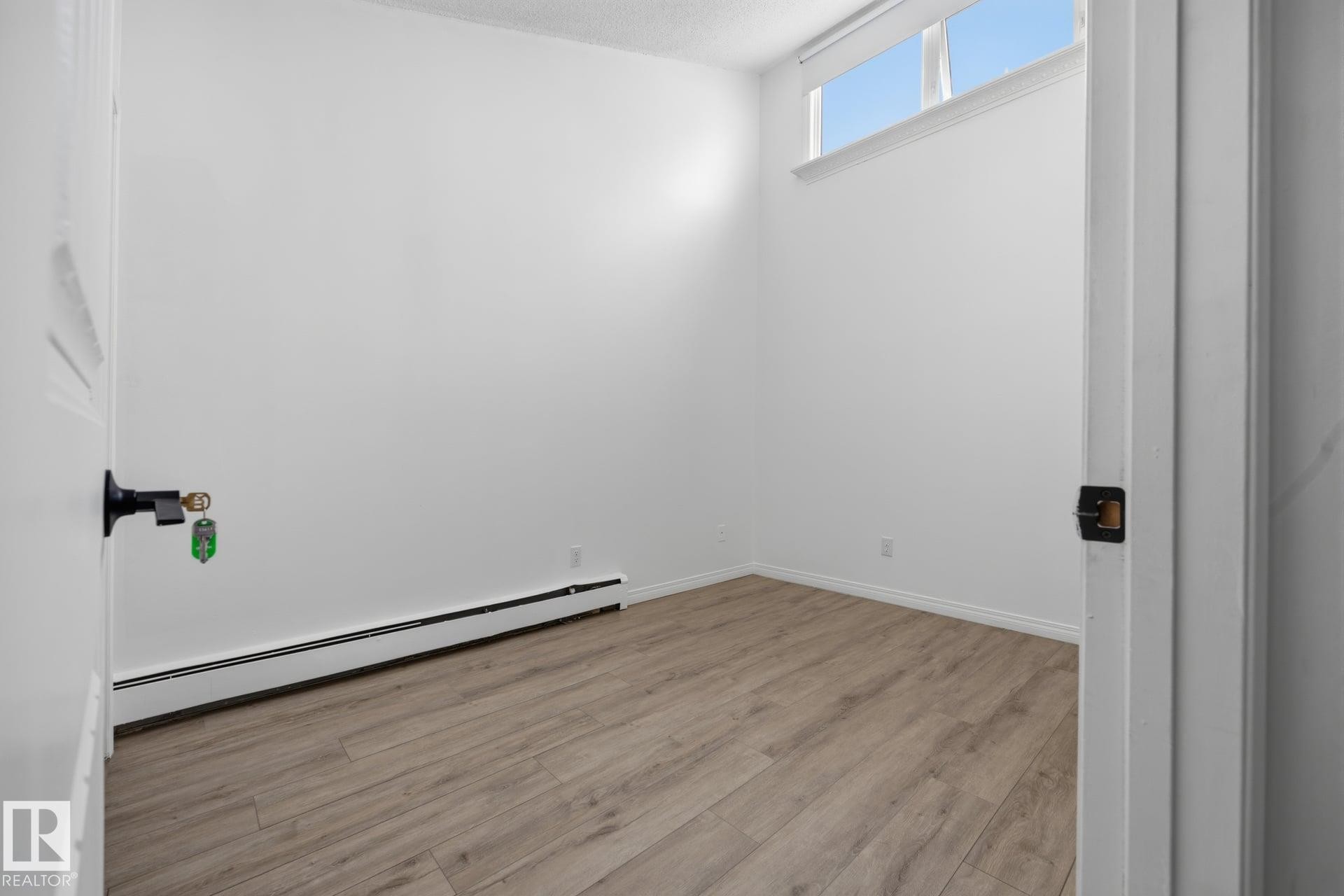 Room featuring wood-finish flooring, white baseboards, and a high transom window - 105 16428 109 Street, Edmonton, AB