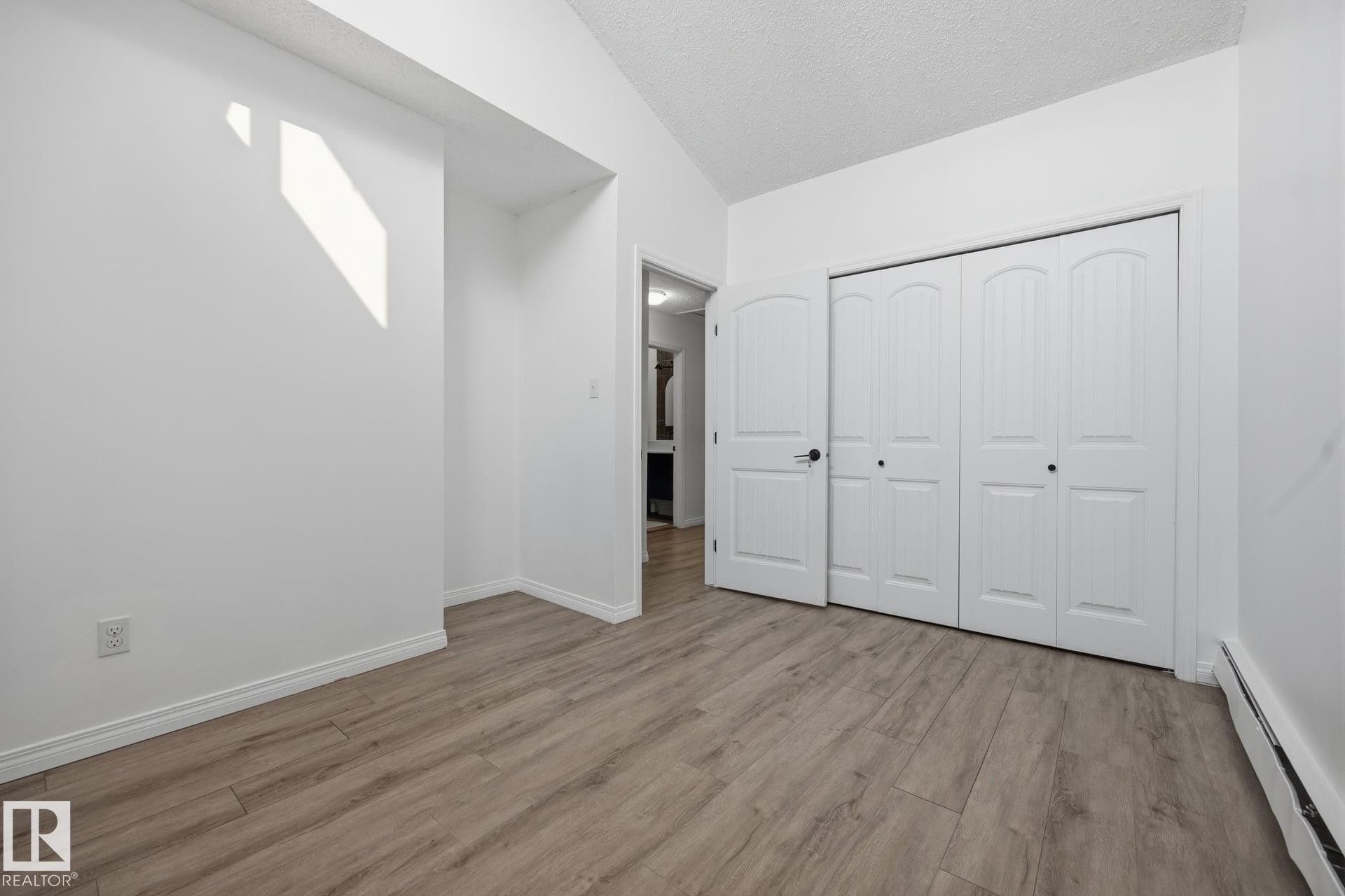 Room featuring wood-finish flooring, white baseboards, and a vaulted ceiling - 105 16428 109 Street, Edmonton, AB
