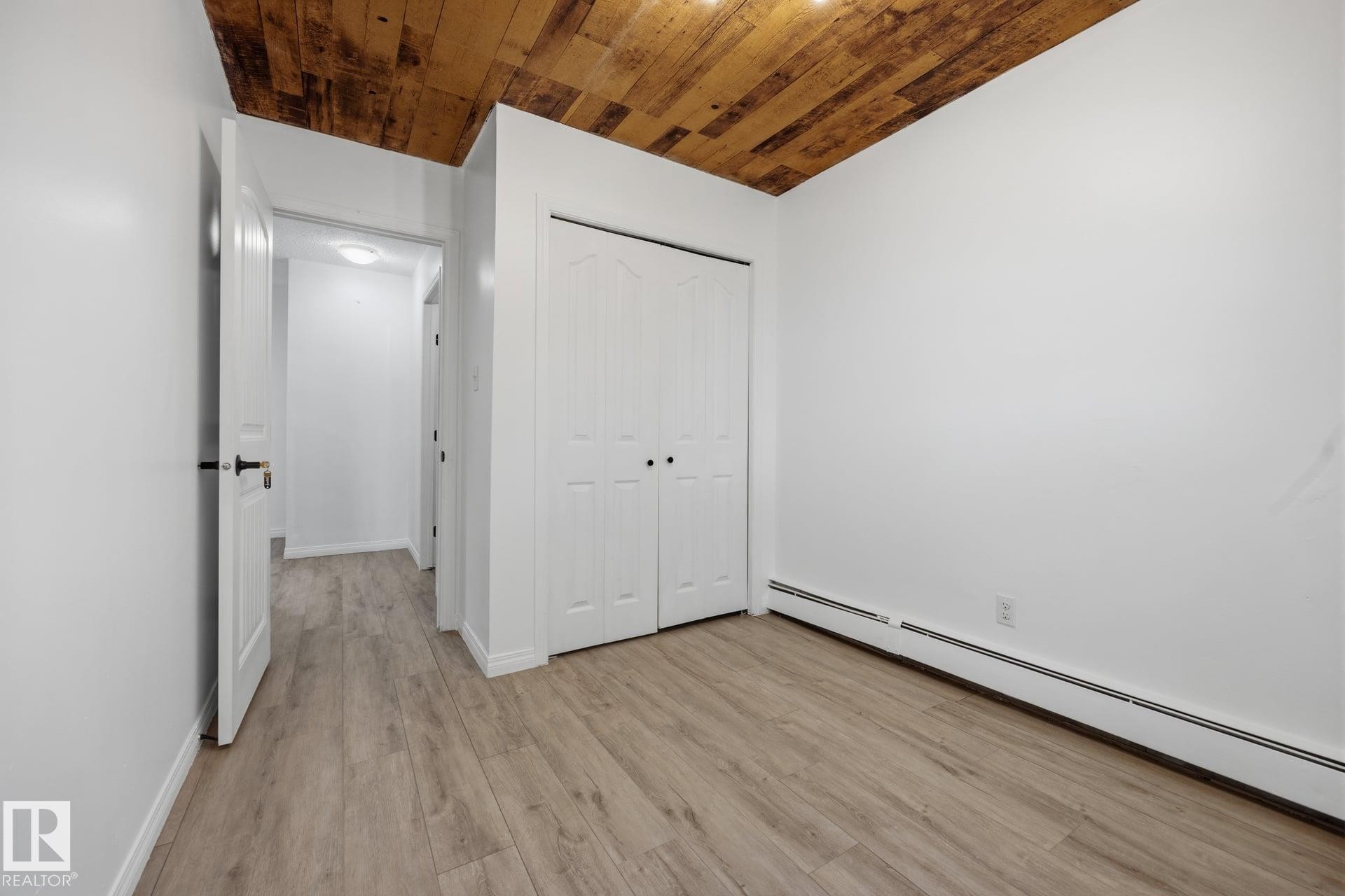 Interior room featuring wood-finish flooring, white walls, and a distinctive wood plank ceiling - 105 16428 109 Street, Edmonton, AB