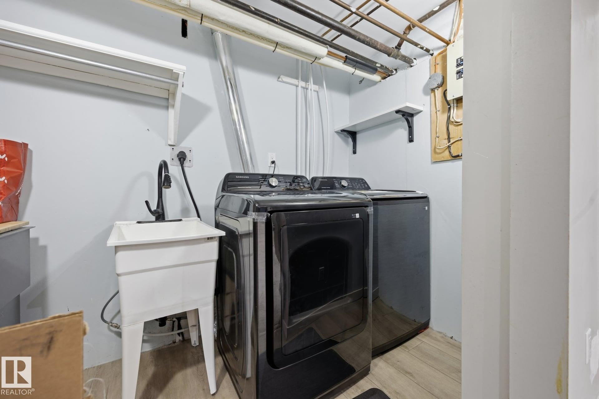 Dedicated laundry area featuring a utility sink with a matte black faucet, light wood-finish flooring, and wall-mounted shelving - 105 16428 109 Street, Edmonton, AB