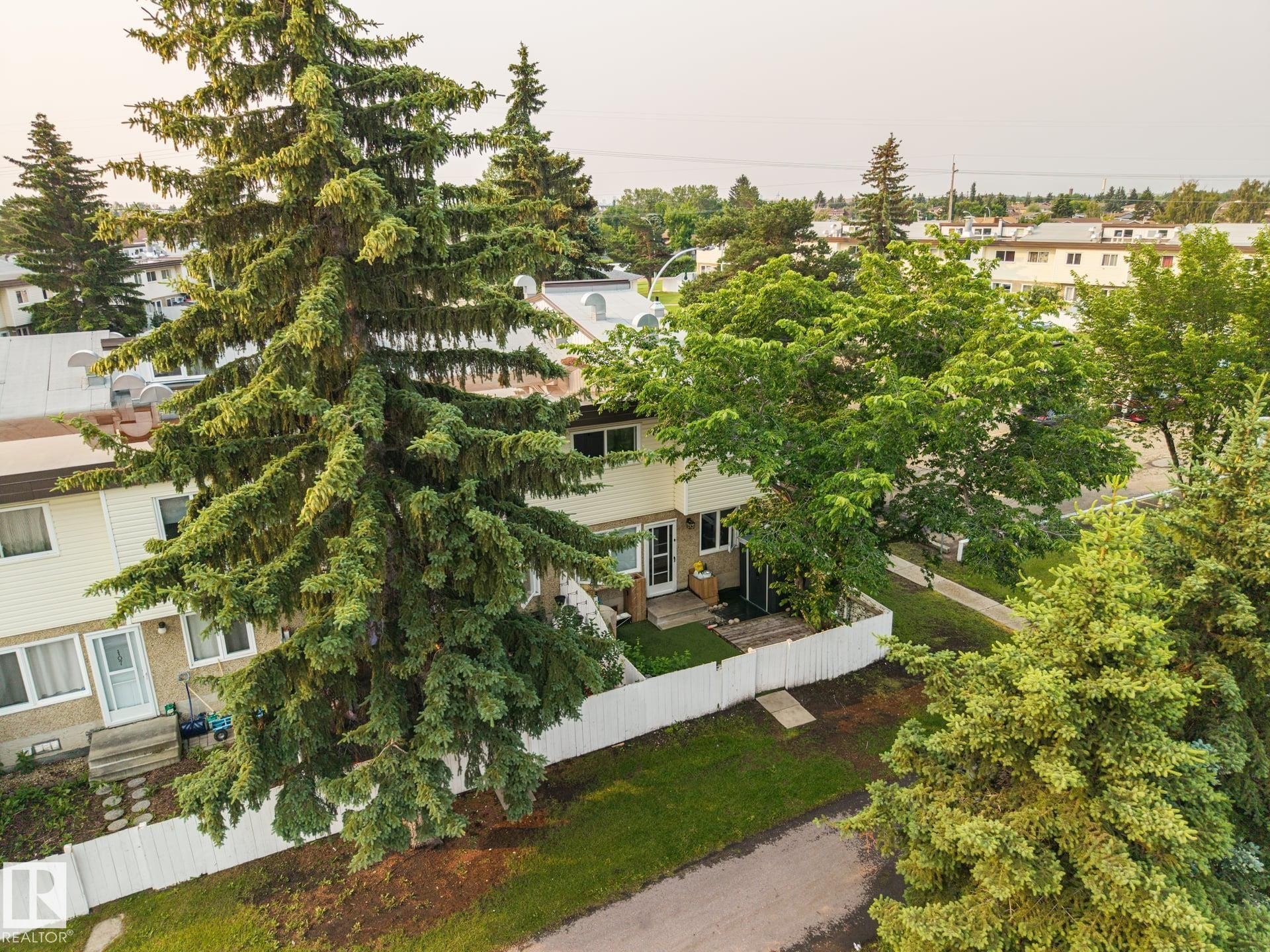 Townhome exterior with light-colored siding and a white picket fence - 105 16428 109 Street, Edmonton, AB