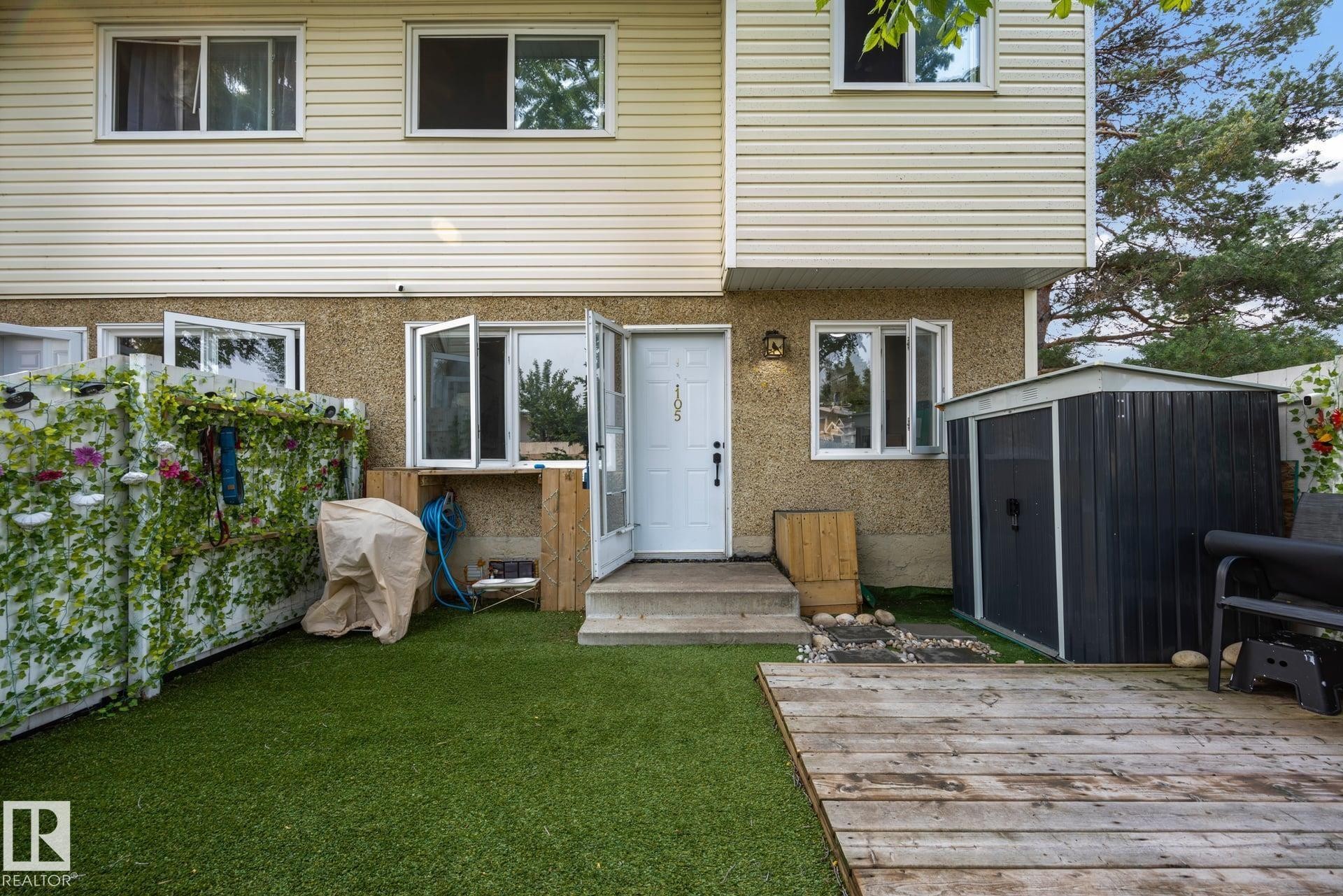 Rear exterior featuring a wood deck, artificial turf, and a storage shed - 105 16428 109 Street, Edmonton, AB