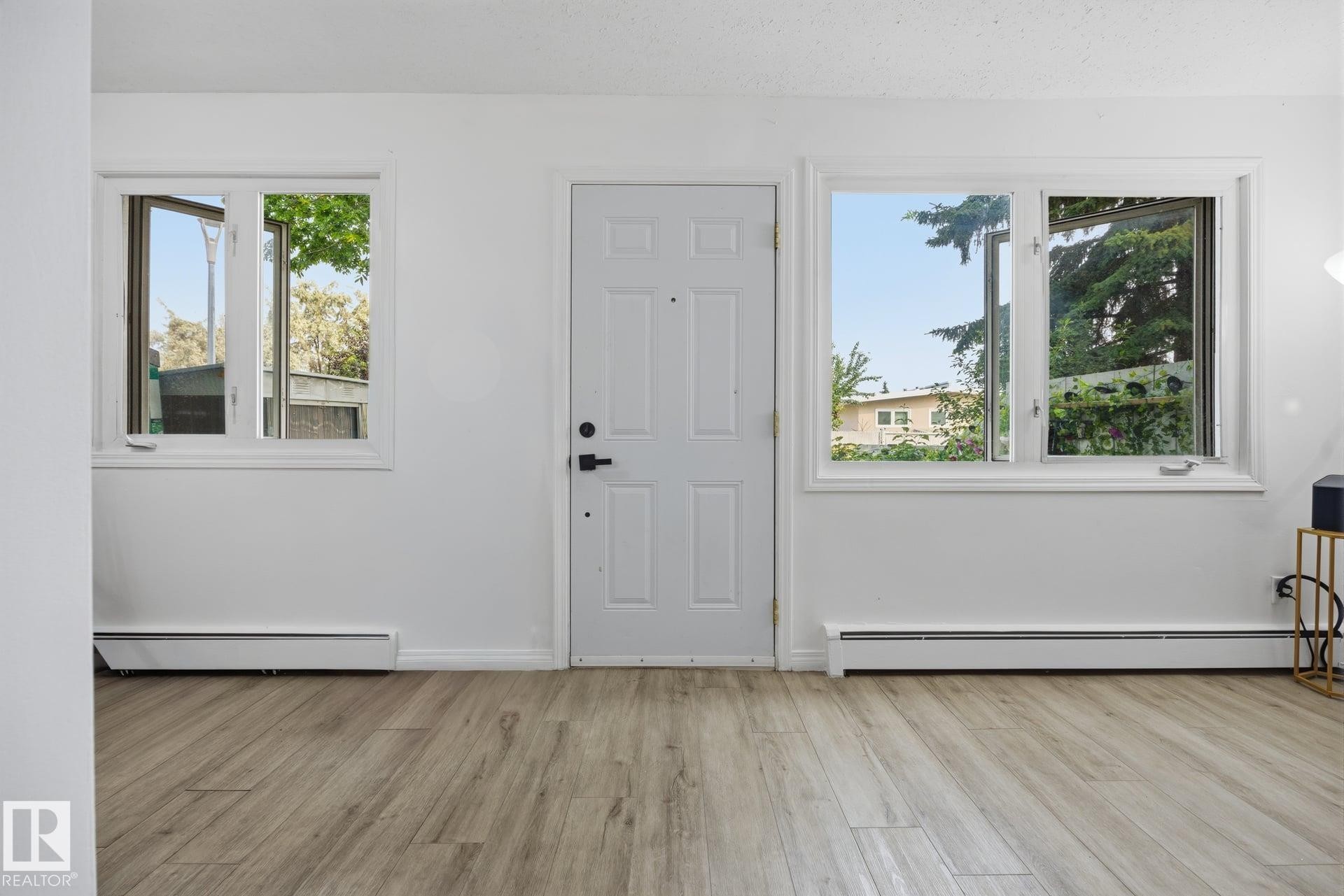 Entryway featuring wood-finish flooring, a paneled door, and two casement windows with white trim - 105 16428 109 Street, Edmonton, AB