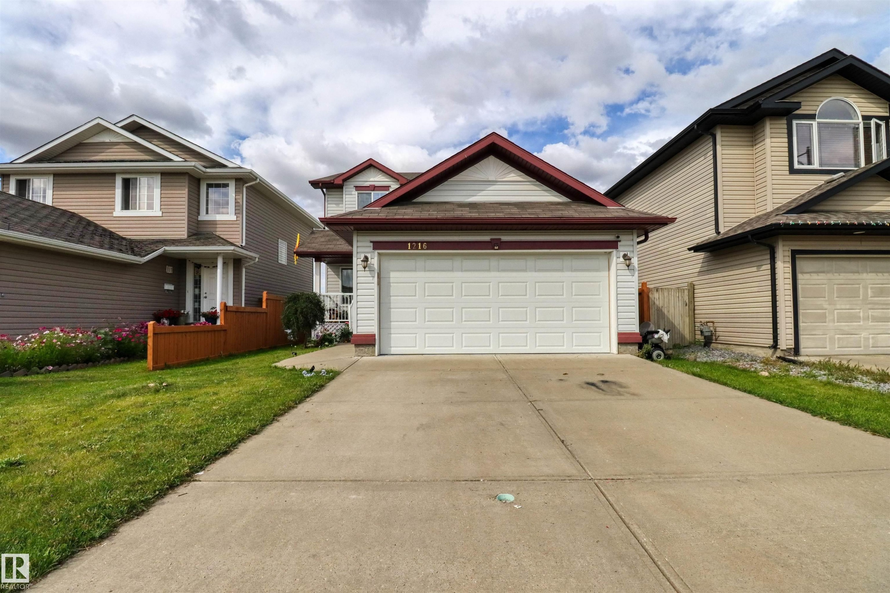 Front exterior featuring light-colored siding with dark trim accents, a prominent white garage door, and a concrete driveway - 1216 37C Avenue Nw, Edmonton, AB - Outdoor With Facade