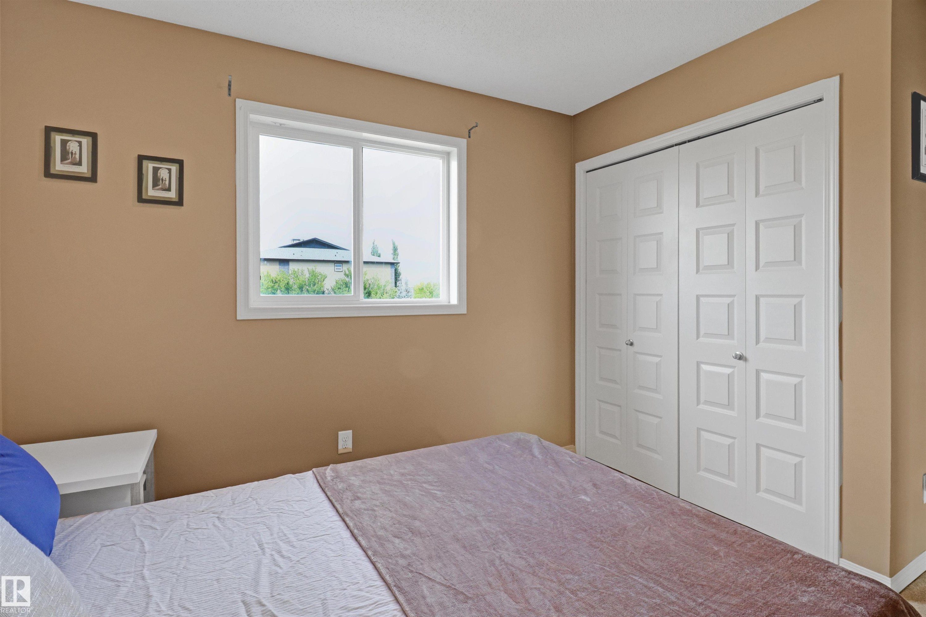 Room featuring a large window with white trim, two sets of white bifold closet doors with square paneling, and neutral-toned walls - 1216 37C Avenue Nw, Edmonton, AB - Indoor Photo Showing Bedroom