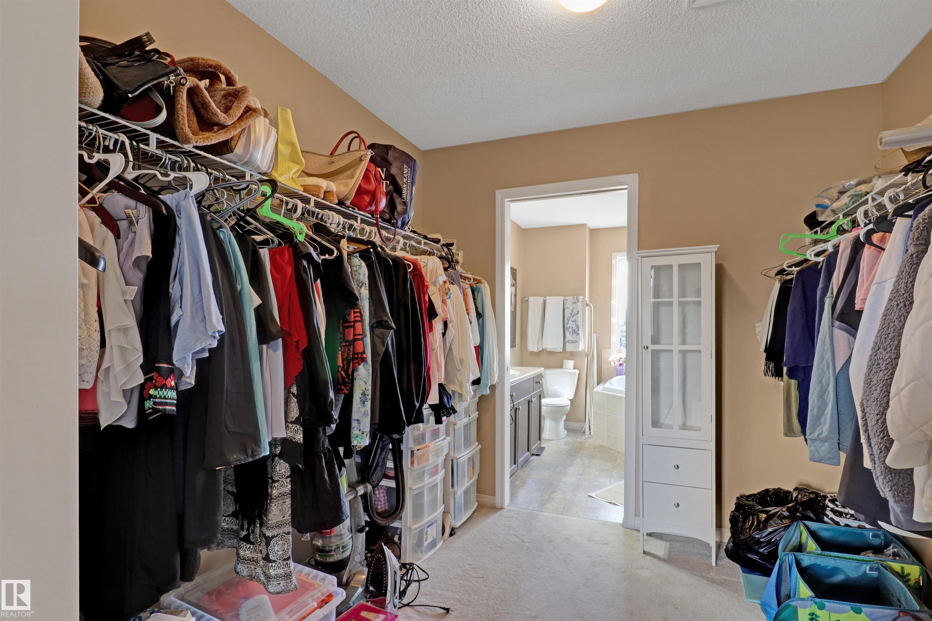 Carpeted walk-in closet featuring wire shelving systems on opposing walls, a built-in white storage cabinet with glass-front doors and two drawers, and direct access to a full bathroom - 1216 37C Avenue Nw, Edmonton, AB - Indoor With Storage