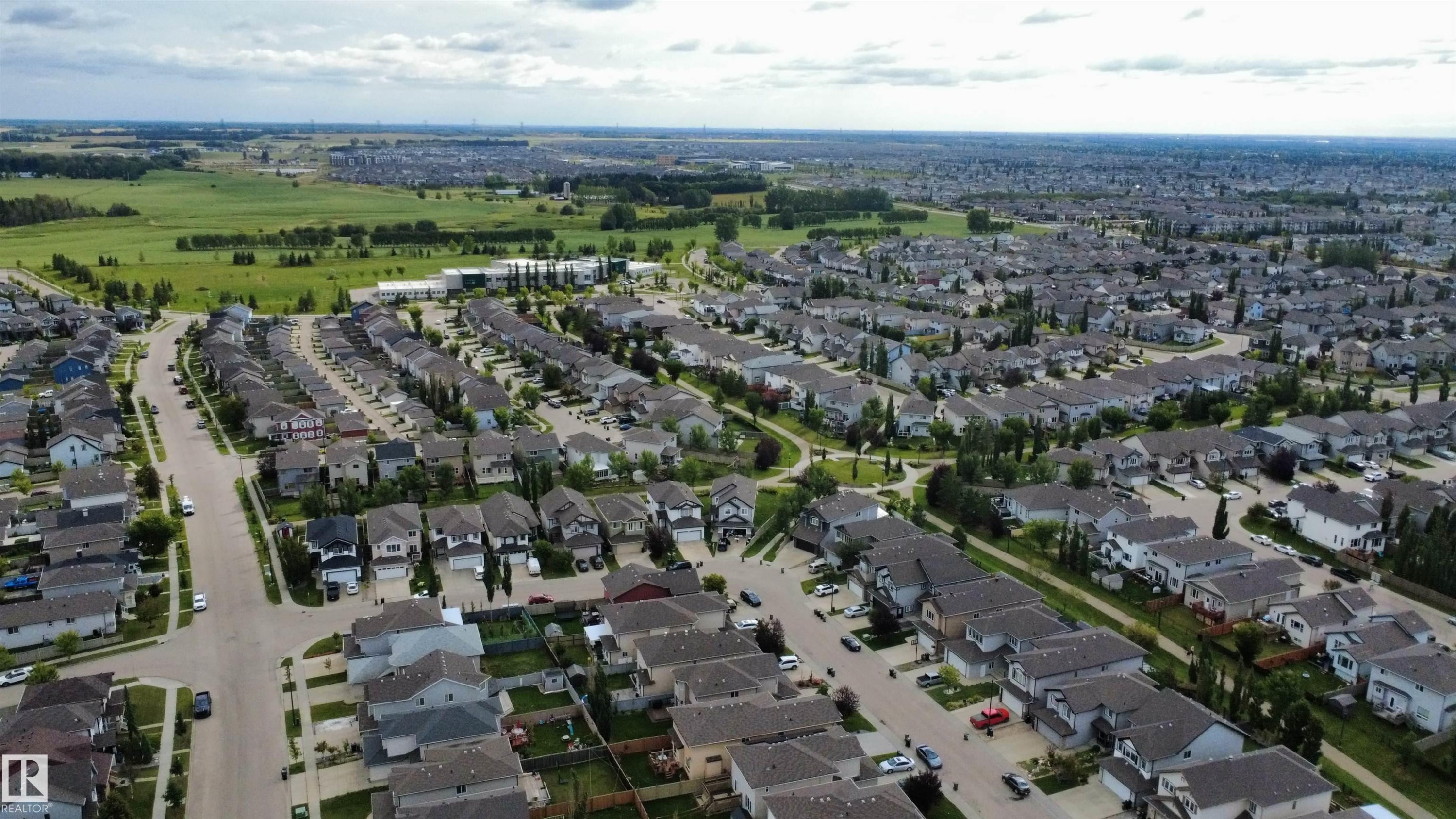 Aerial perspective showcasing a residential neighborhood with numerous single-family homes, paved streets, and a backdrop of open green fields - 1216 37C Avenue Nw, Edmonton, AB - Outdoor With View