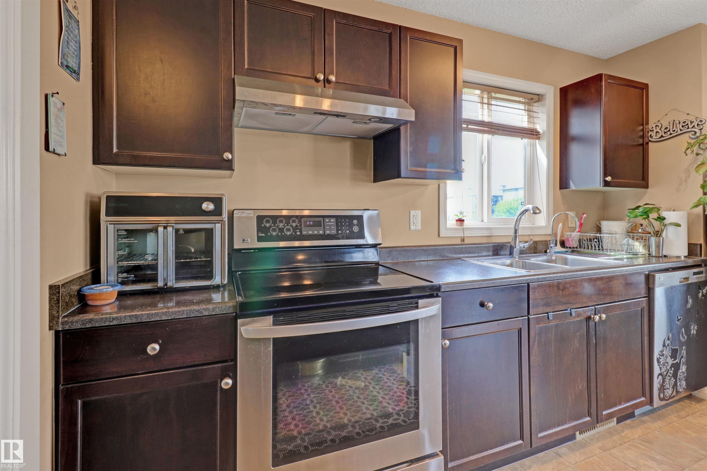 Kitchen featuring dark wood-finish cabinetry, a stainless steel range with overhead ventilation, and a double basin sink - 1216 37C Avenue Nw, Edmonton, AB - Indoor Photo Showing Kitchen With Double Sink