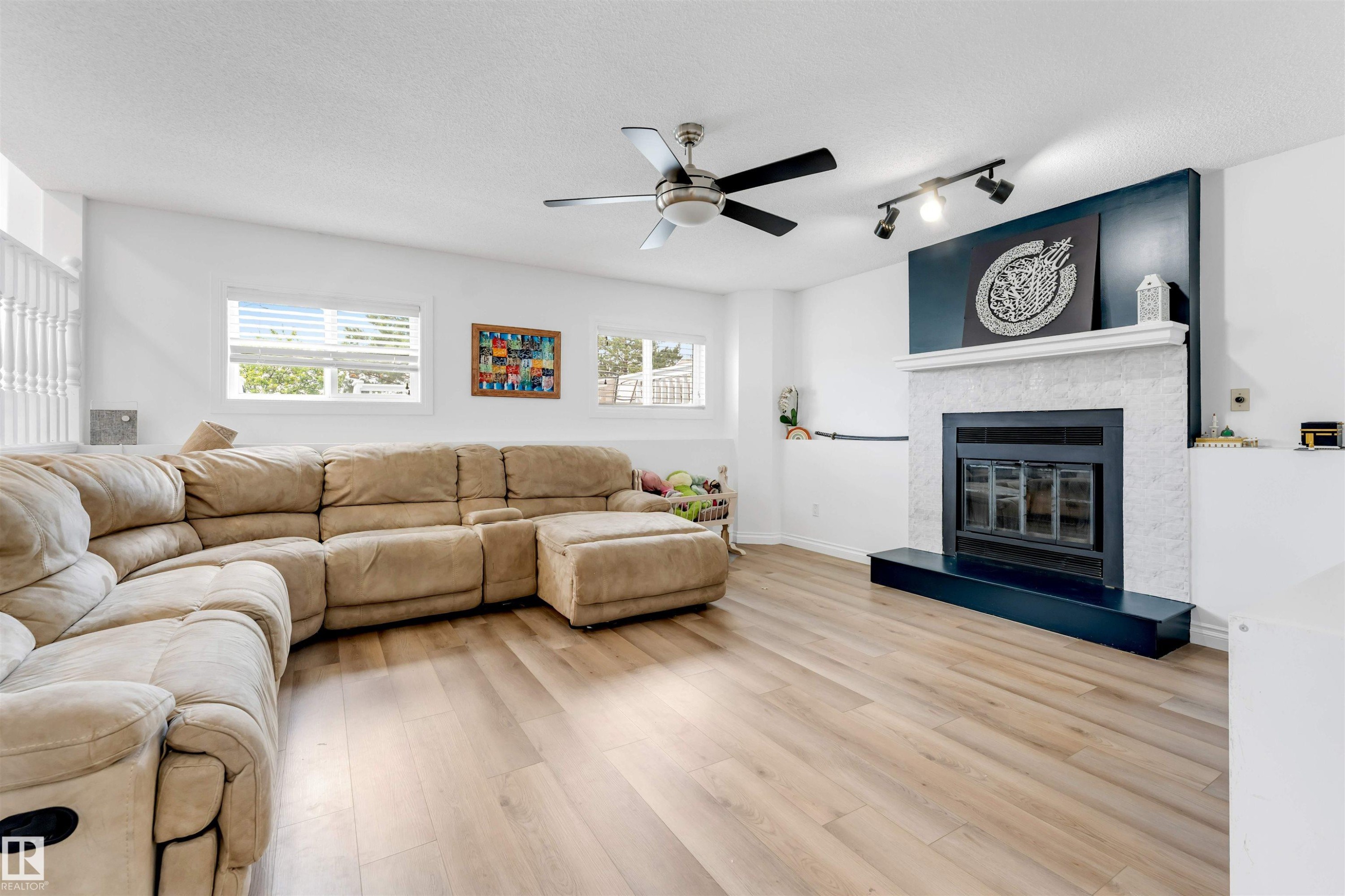 Spacious room featuring wood-finish flooring, multiple windows with blinds, and a ceiling fan - 3332 43 Street Nw, Edmonton, AB
