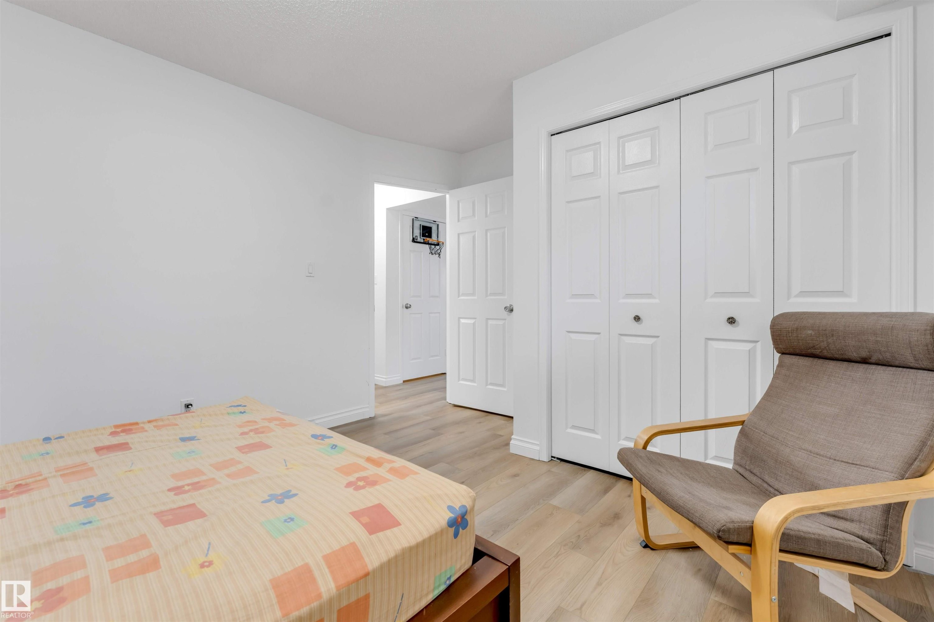 Room featuring wood-finish flooring, white walls, and bi-fold closet doors - 3332 43 Street Nw, Edmonton, AB
