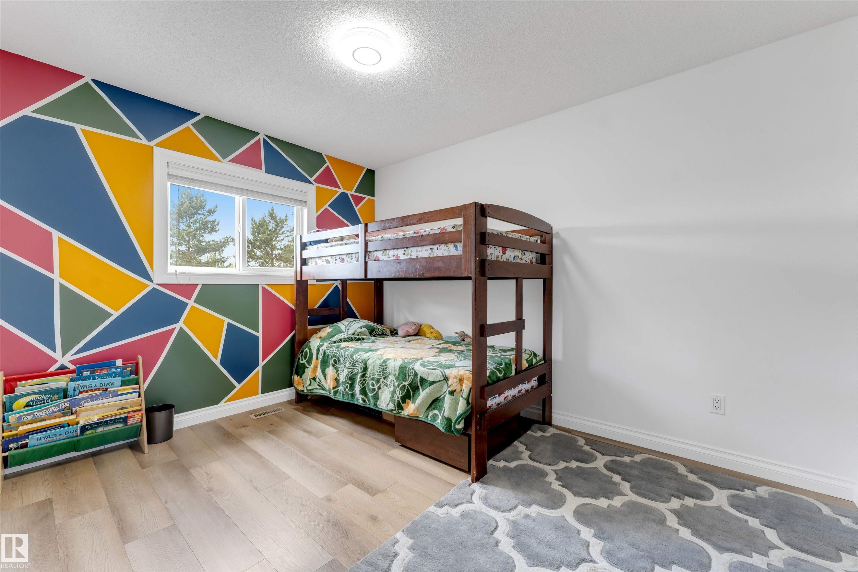 Room featuring a geometric accent wall with vibrant colors, light wood-finish flooring, and a white ceiling with a flush-mount light fixture - 3332 43 Street Nw, Edmonton, AB